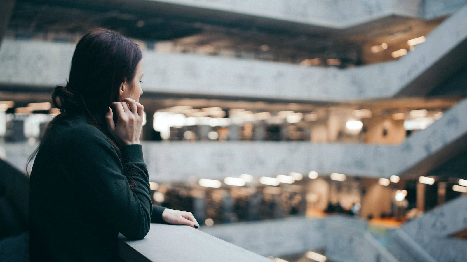 Lonely 桌布 壁紙 — 一位身穿深色外套的女性從現代建築風格的陽台沉思地俯瞰多層室內空間。