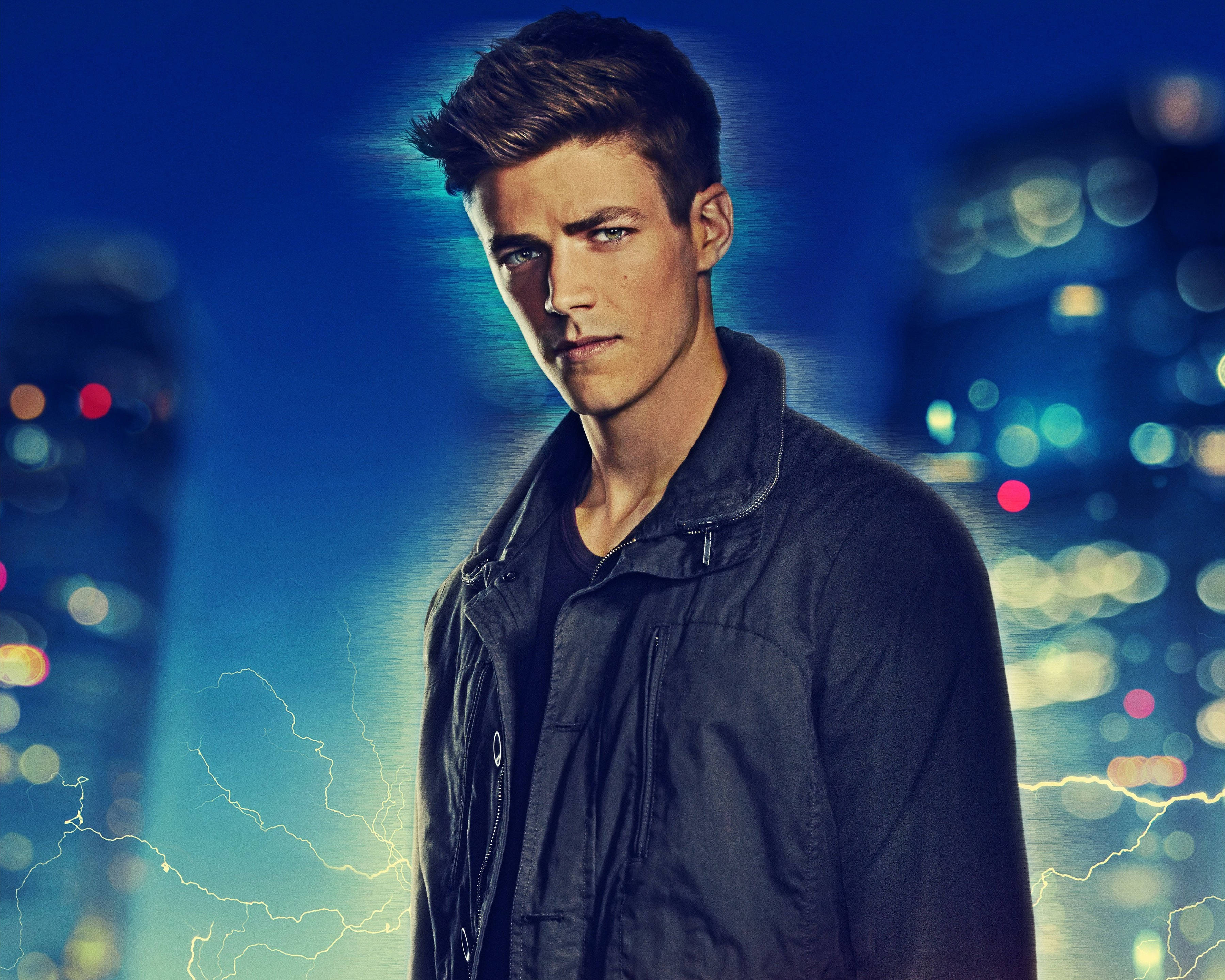 Grant Gustin 桌布 壁紙 — 一位身穿深色外套的年輕男子，在夜晚以充滿活力的藍色城市景觀為背景，伴隨著發光的散景燈光和電光效果。