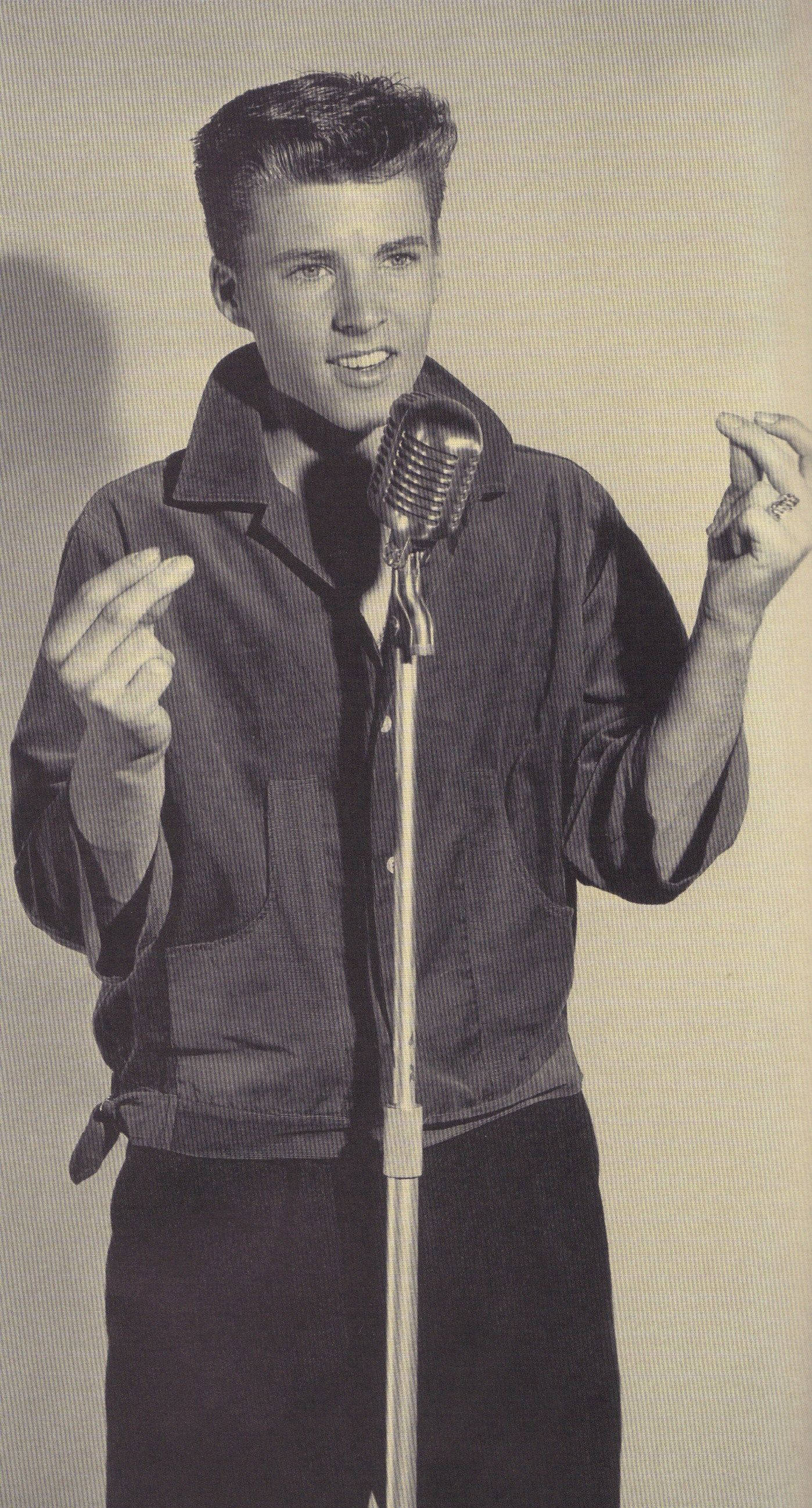 Singer 桌布 壁紙 — 一位身穿深色外套的年輕男子站在復古麥克風前，在錄音室環境中表情豐富地做手勢。