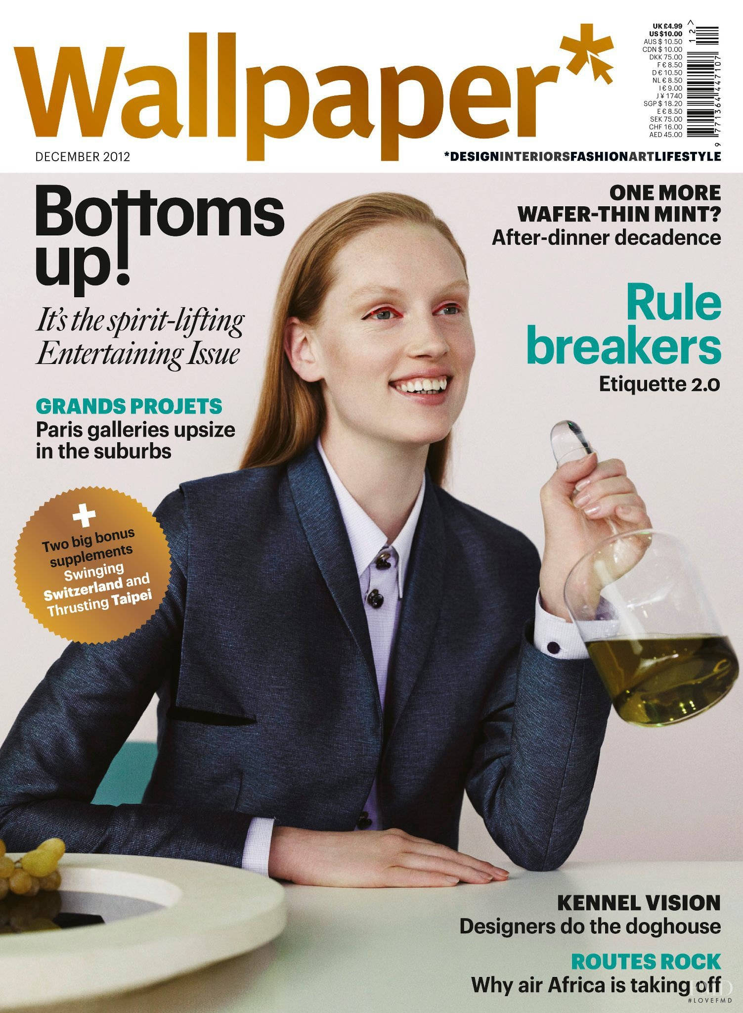 雜誌 桌布 壁紙 — 一位身穿深色西裝、面帶微笑的女性，在放有葡萄的白色桌子上拿著一杯琥珀色液體。