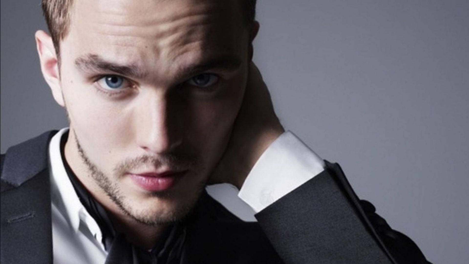 Nicholas Hoult 桌布 壁紙 — 一位身穿深色西裝和白色襯衫的男士特寫肖像，強烈的藍色眼睛直視鏡頭。