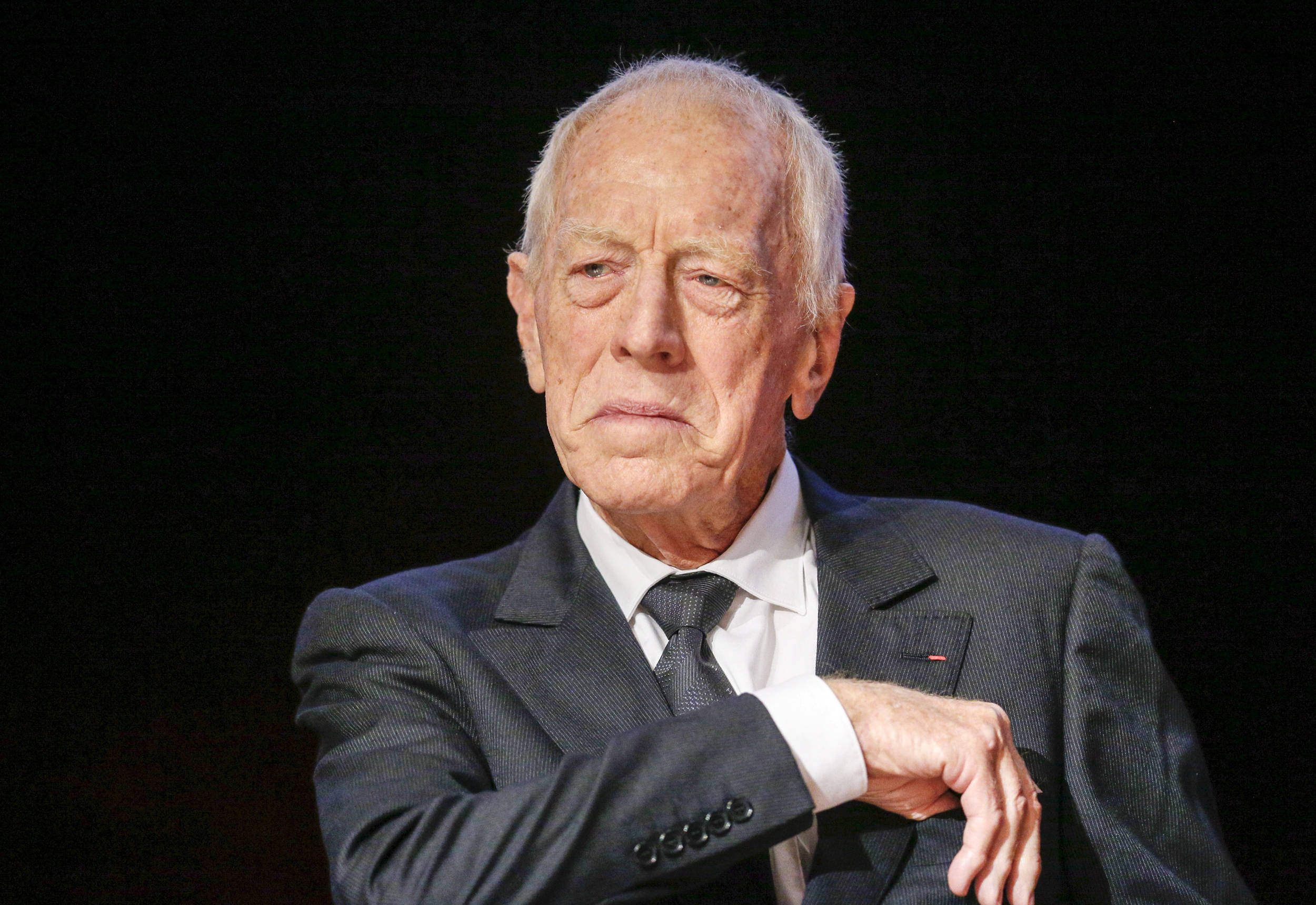 actor 桌布 壁紙 — 一位身穿深色西裝和領帶的長者，在黑色背景前若有所思地凝視，柔和的光線突顯他飽經風霜的面容。