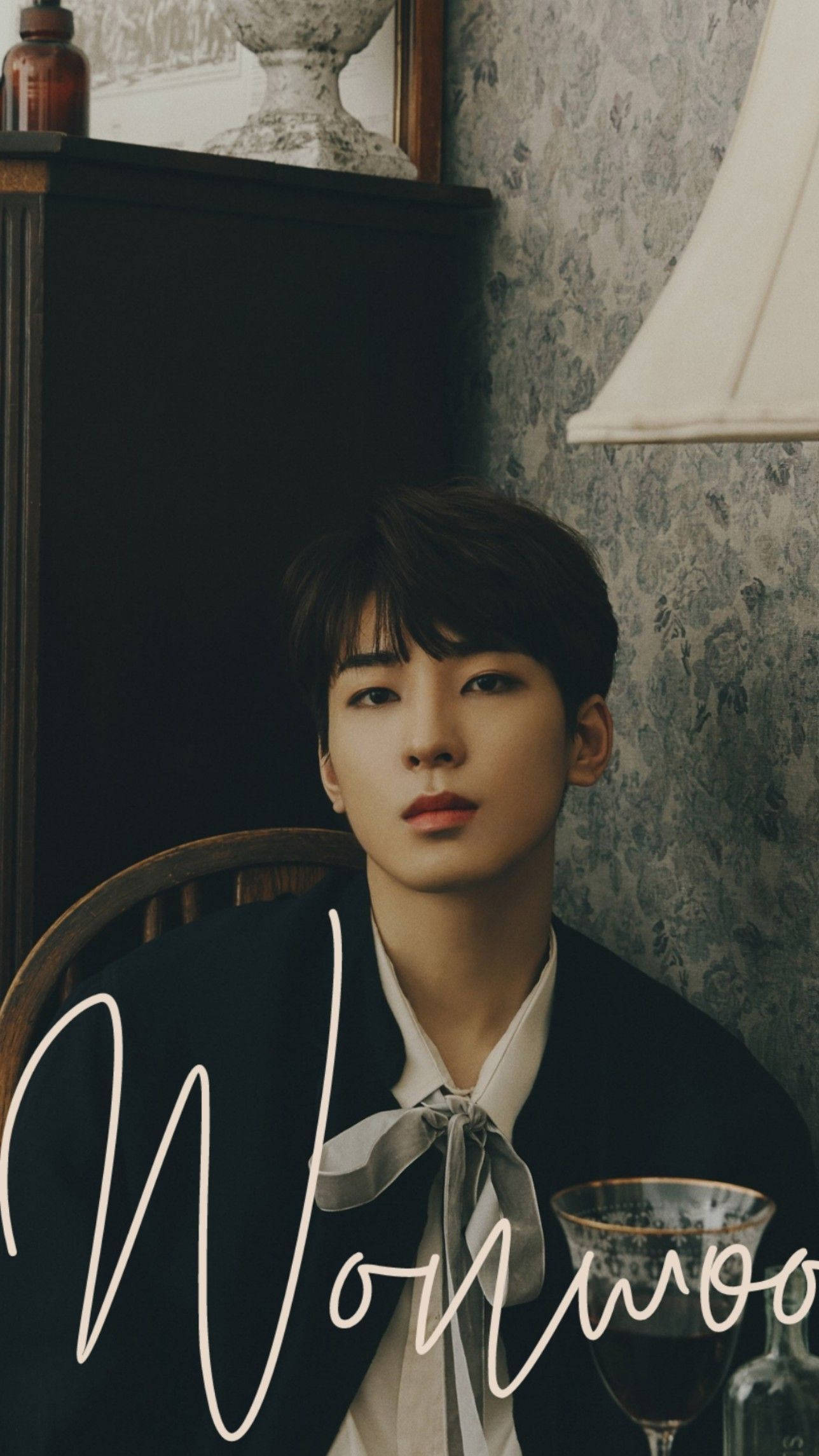 원우 桌布 壁紙 — 一位身穿深色西裝外套和領結的年輕男子坐在木椅上，背景是復古花卉壁紙牆壁，附近有燈和玻璃杯。