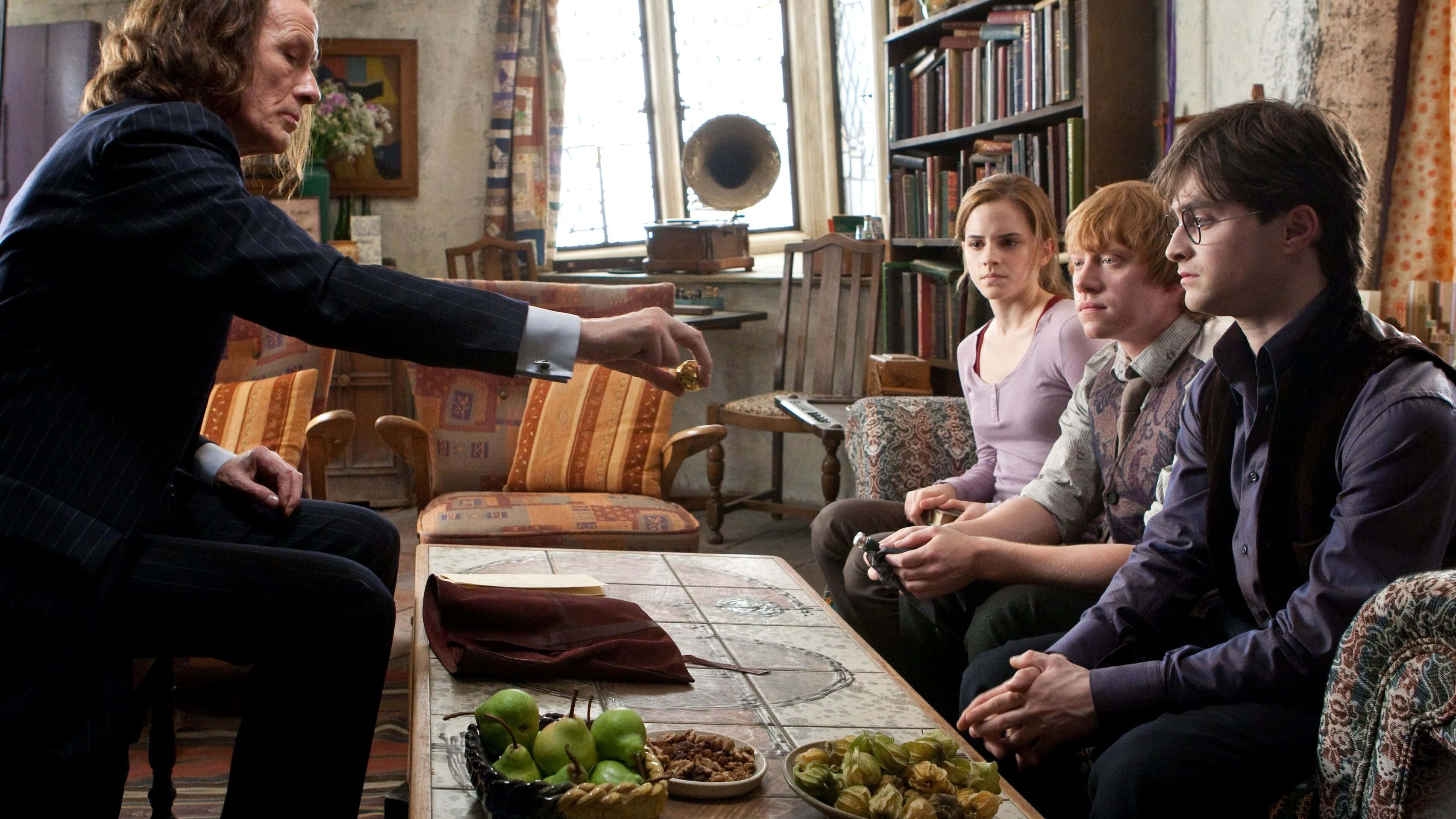 Harry Potter 4K 桌布 壁紙 — 一位身穿深色西裝的巫師向三位坐在舒適、充滿書籍的房間裡的學生做手勢，房間裡有復古家具和自然光線。