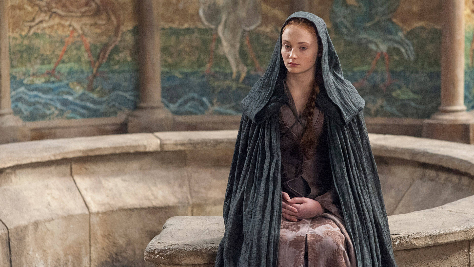 Sansa Stark 桌布 壁紙 — 一位身穿深色連帽斗篷的年輕女子莊嚴地坐在石凳上，身後是帶有彩繪壁畫的古老柱子。
