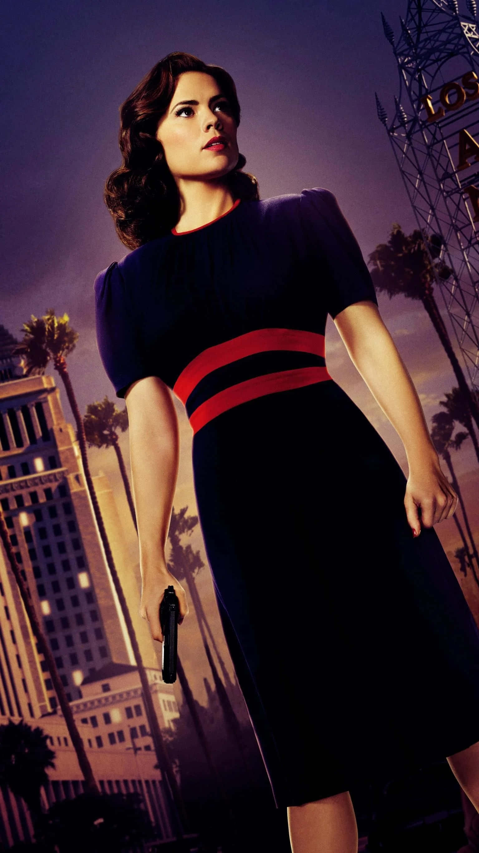 Peggy Carter 桌布 壁紙 — 一位身穿深色連衣裙、繫著紅色腰帶的女性，在暮色城市景觀中手持槍支，背景有棕櫚樹和「洛杉磯」標誌。