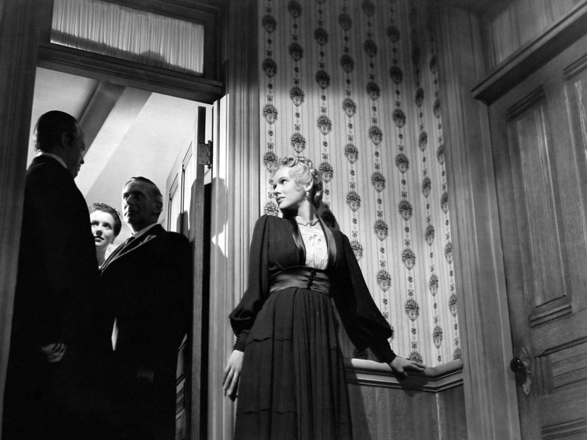 Citizen Kane 桌布 壁紙 — 一位身穿深色連衣裙的女子站在門口，門框由圖案壁紙裝飾，三位身穿西裝的男子在戲劇性的黑白場景中注視著。