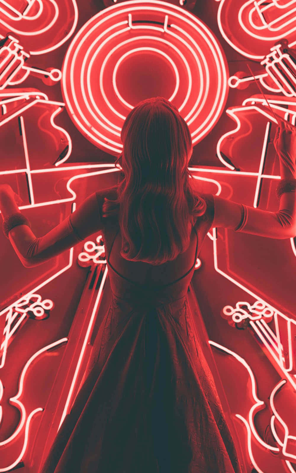 Red Light 桌布 壁紙 — 一位身穿深色連衣裙的女性張開雙臂，面向一面裝飾著樂器輪廓的發光紅色霓虹牆。