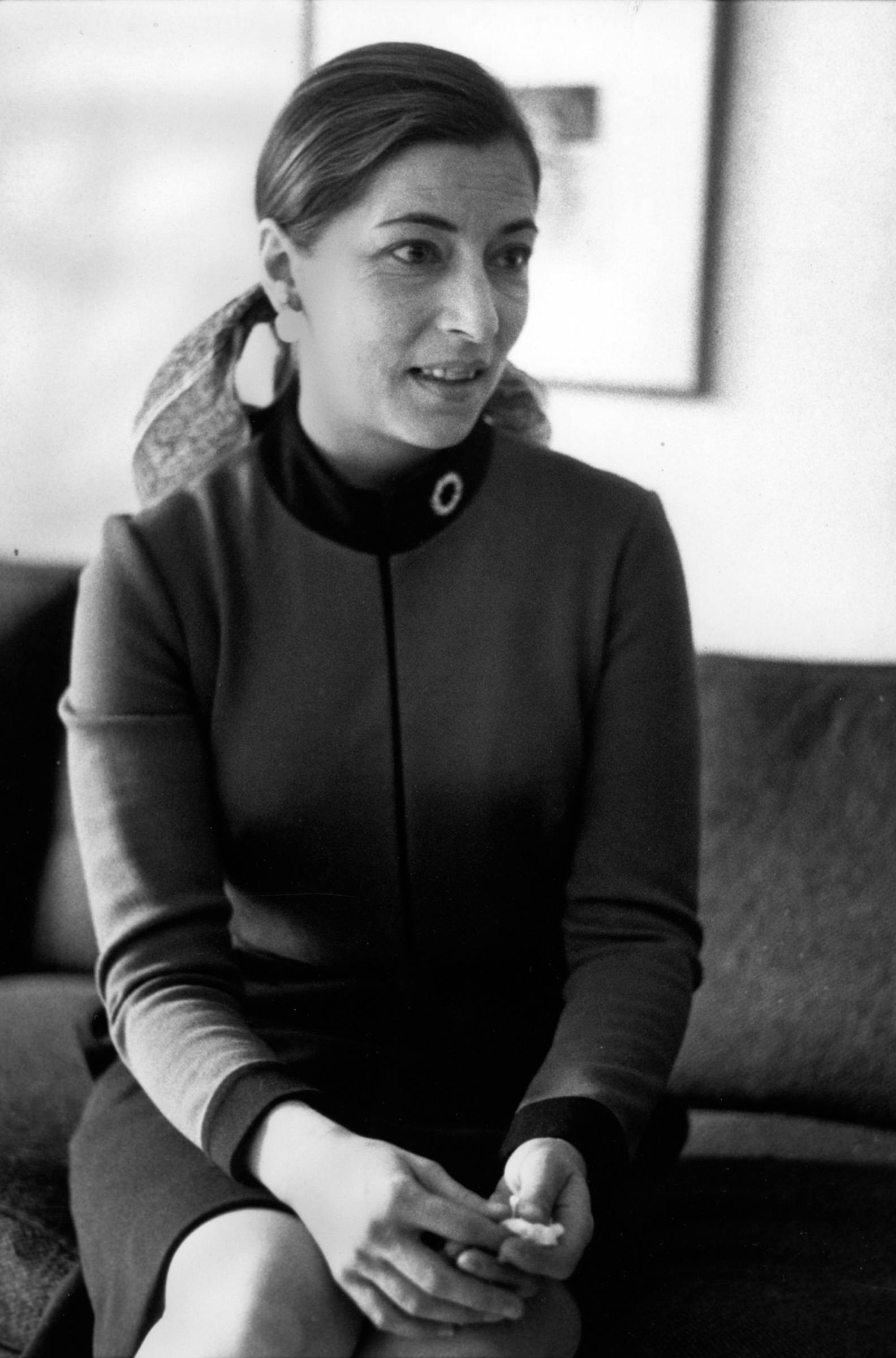 Ruth Bader Ginsburg 桌布 壁紙 — 一位身穿深色連衣裙的女性雙手交握坐在沙發上，在復古黑白照片中看向鏡頭外。