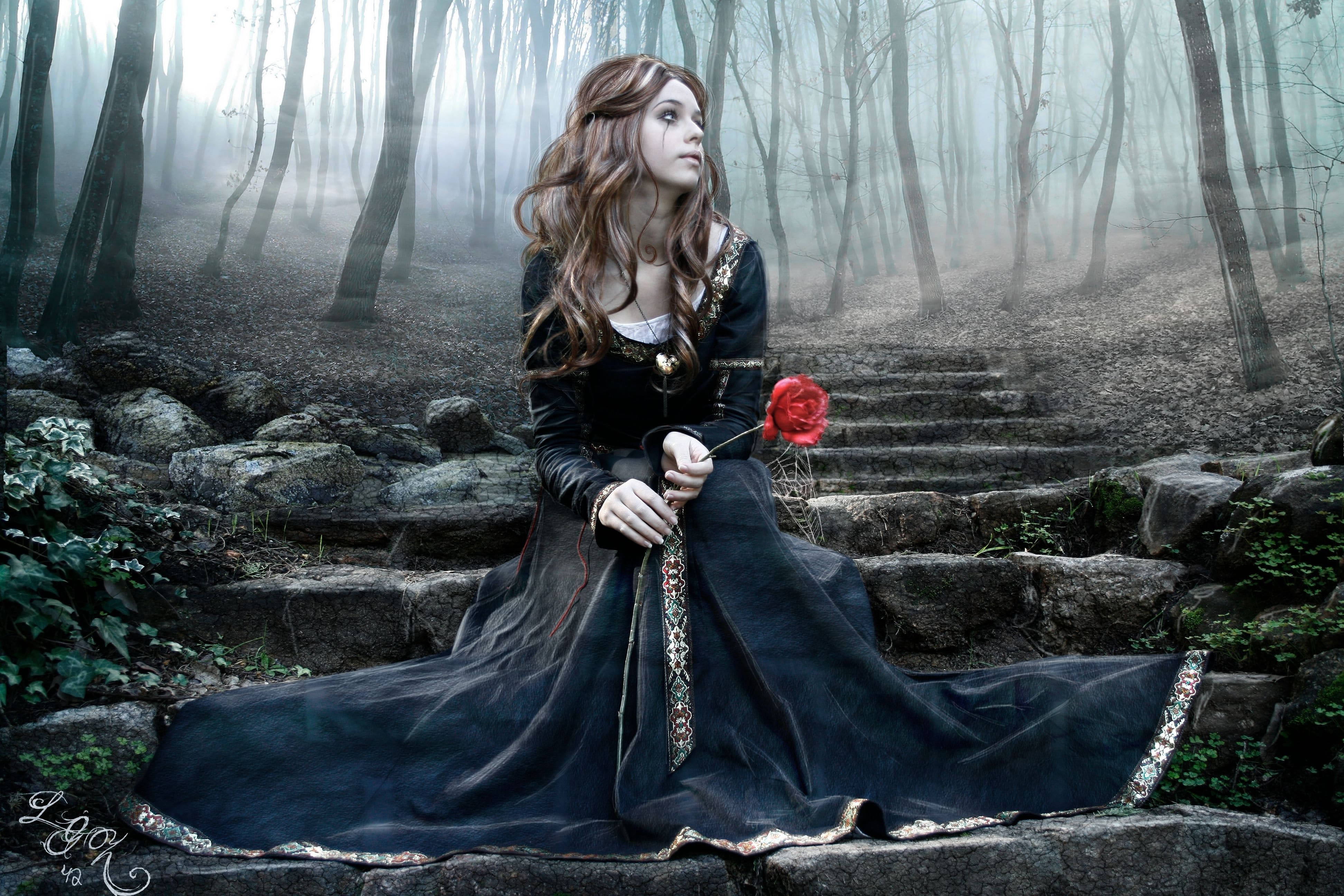 Goth 桌布 壁紙 — 一位身穿深色長袍的女子坐在霧氣瀰漫的森林中的石階上，手持一朵紅玫瑰。