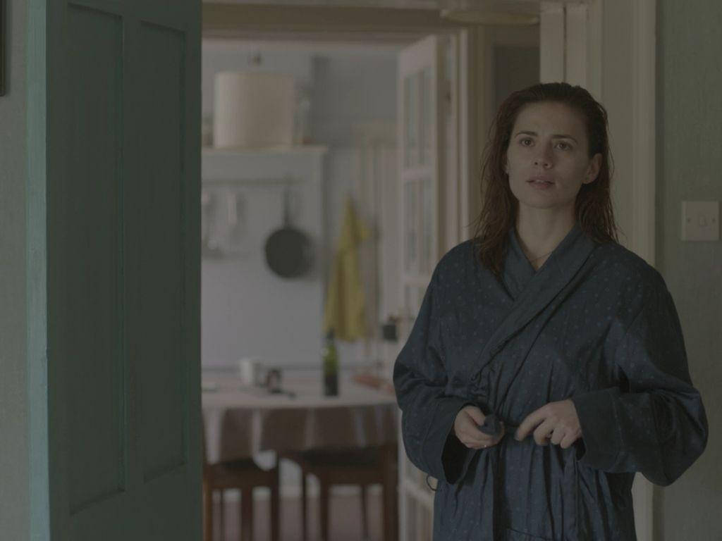 Netflix 桌布 壁紙 — 一位身穿深色長袍的女性站在燈光昏暗的走廊裡，表情嚴肅地看向鏡頭。