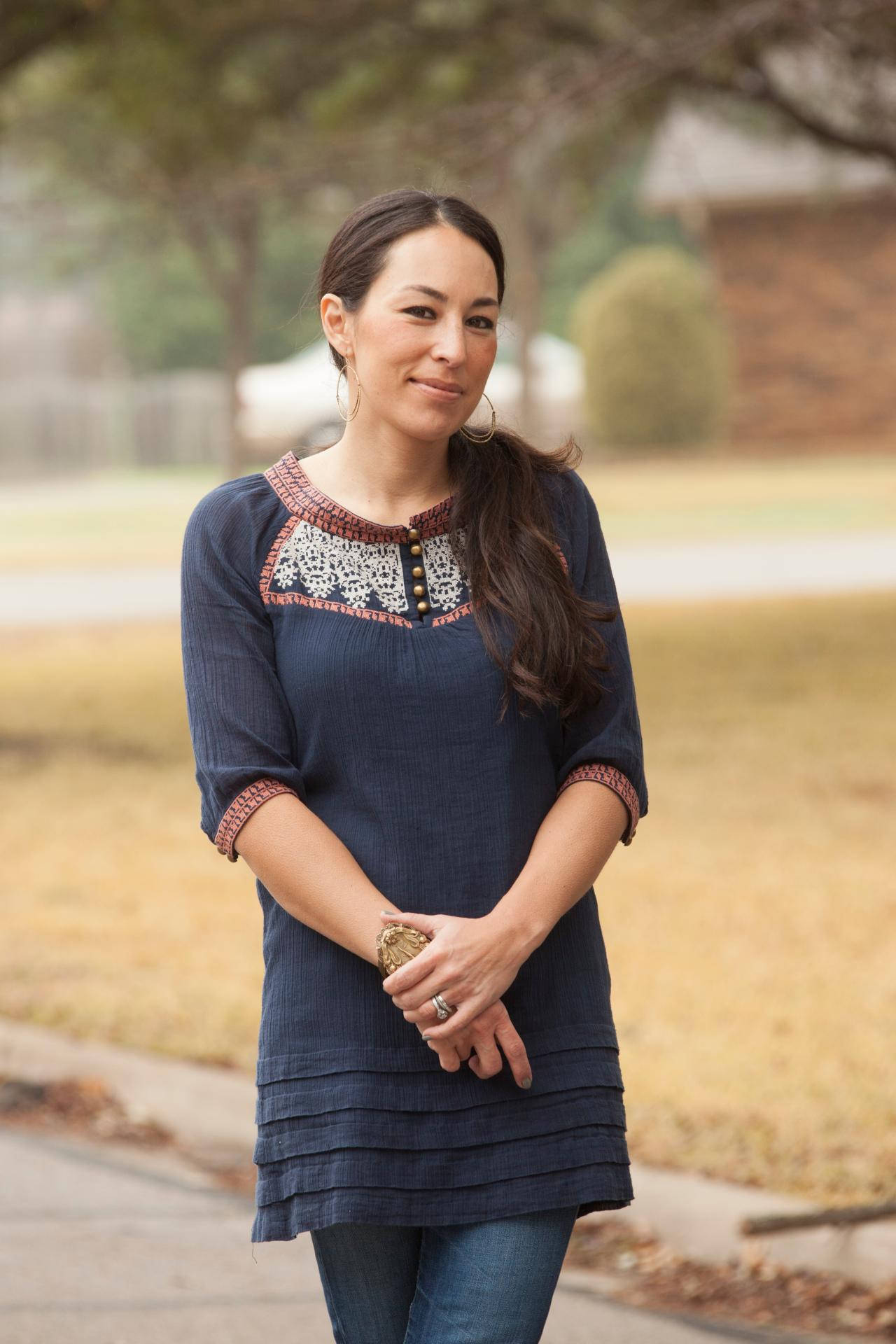 Joanna 桌布 壁紙 — 一位身穿深藍色刺繡上衣的女性站在戶外的人行道上，背景有乾草和樹木。