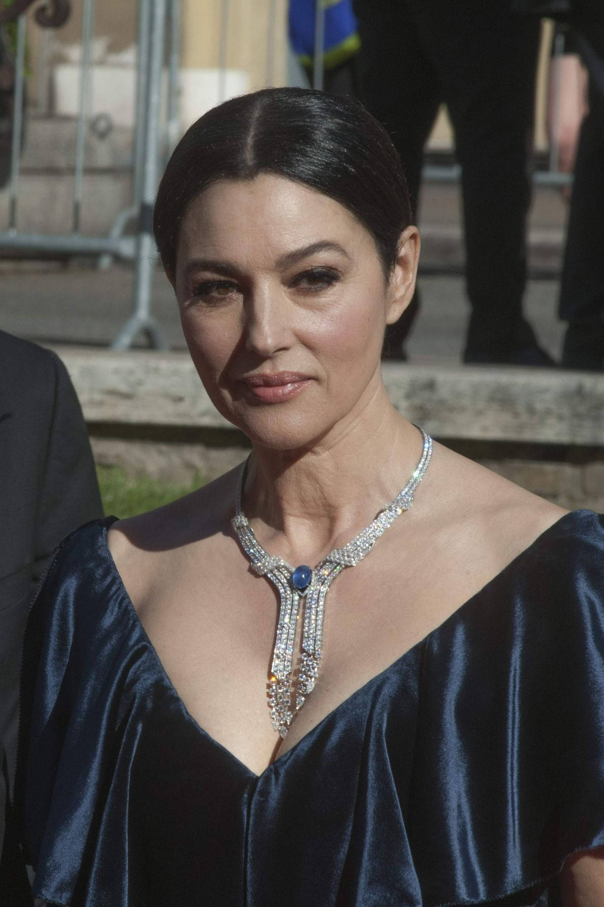 monica bellucci 桌布 壁紙 — 一位身穿深藍色天鵝絨連衣裙的女性在明亮的日光下佩戴著精緻的鑽石和藍寶石項鍊。