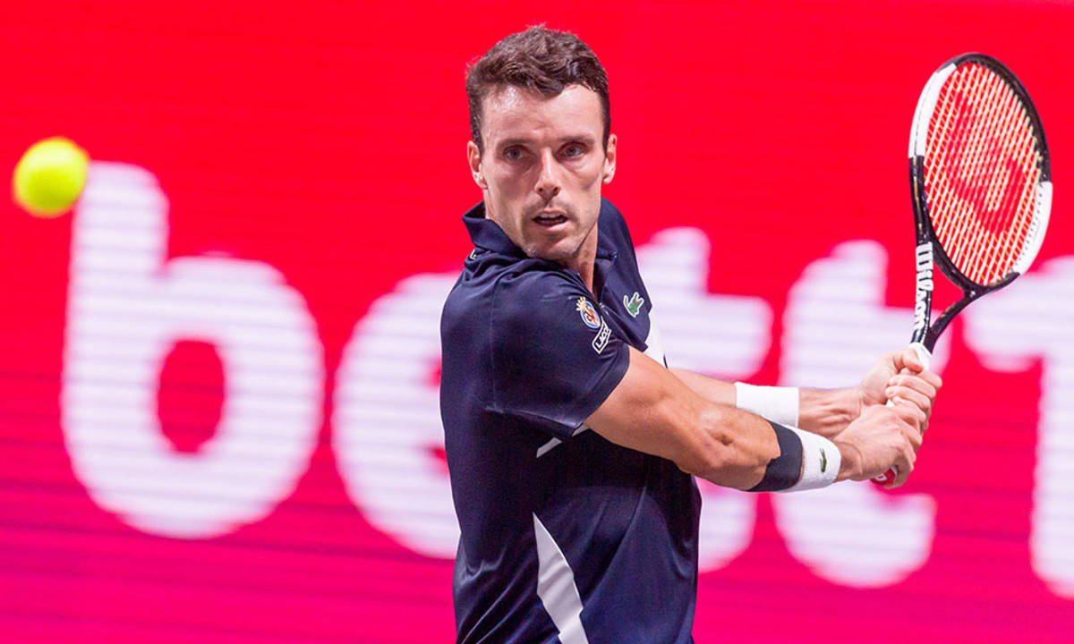 Tennis 桌布 壁紙 — 一位身穿深藍色襯衫的男性網球運動員在明亮的紅色背景上，帶有白色字體，揮拍擊打黃色網球。