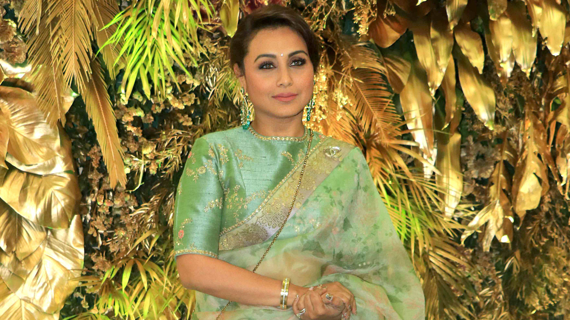 Rani Mukerji 桌布 壁紙 — 一位身穿淺綠色刺繡紗麗的女性，優雅地站在華麗的金色和綠色葉子背景前。