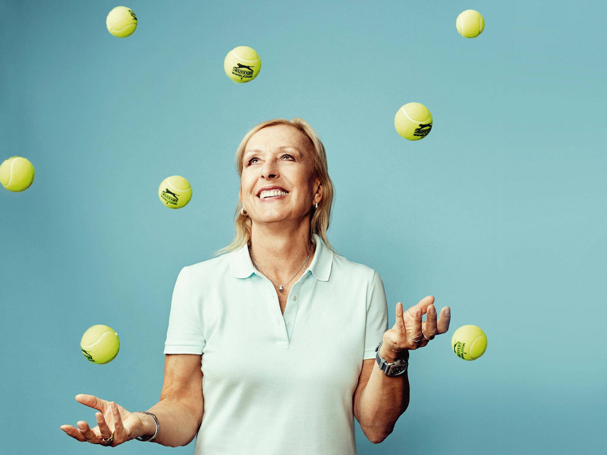 Martina Navratilova 桌布 壁紙 — 一位身穿淺色Polo衫的快樂女性，在純藍色背景前微笑著拋接亮黃色的網球。