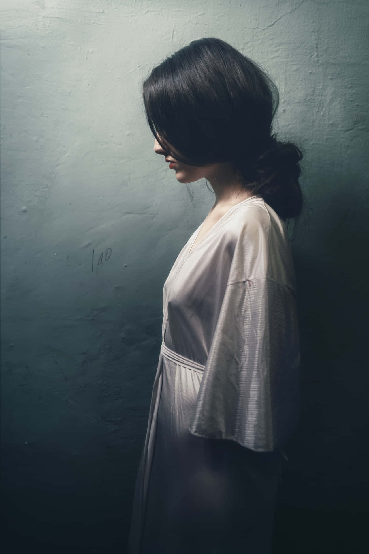 Woman 桌布 壁紙 — 一位身穿淺色長袍的女性側身站在有紋理的青綠色牆壁前，沐浴在柔和側光中。