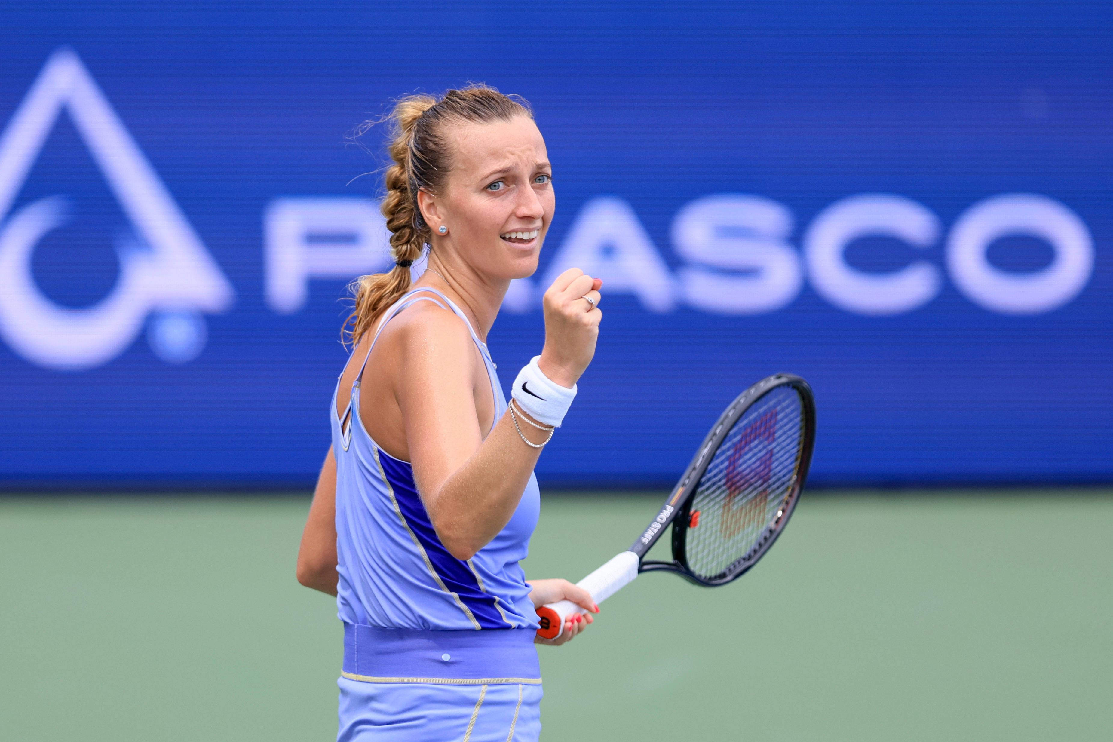 Tennis 桌布 壁紙 — 一位身穿淺藍色服裝的女網球選手在綠色球場上，以藍色贊助商背景為襯托，握緊拳頭慶祝。