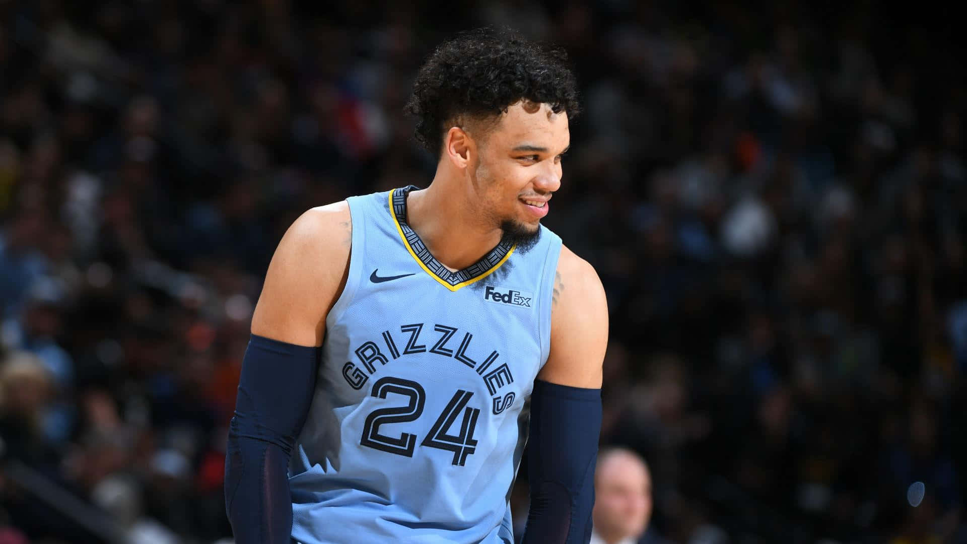 Dillon Brooks 桌布 壁紙 — 一位身穿淺藍色灰熊隊球衣的籃球運動員站在球場上，身後是模糊的人群，面帶微笑。