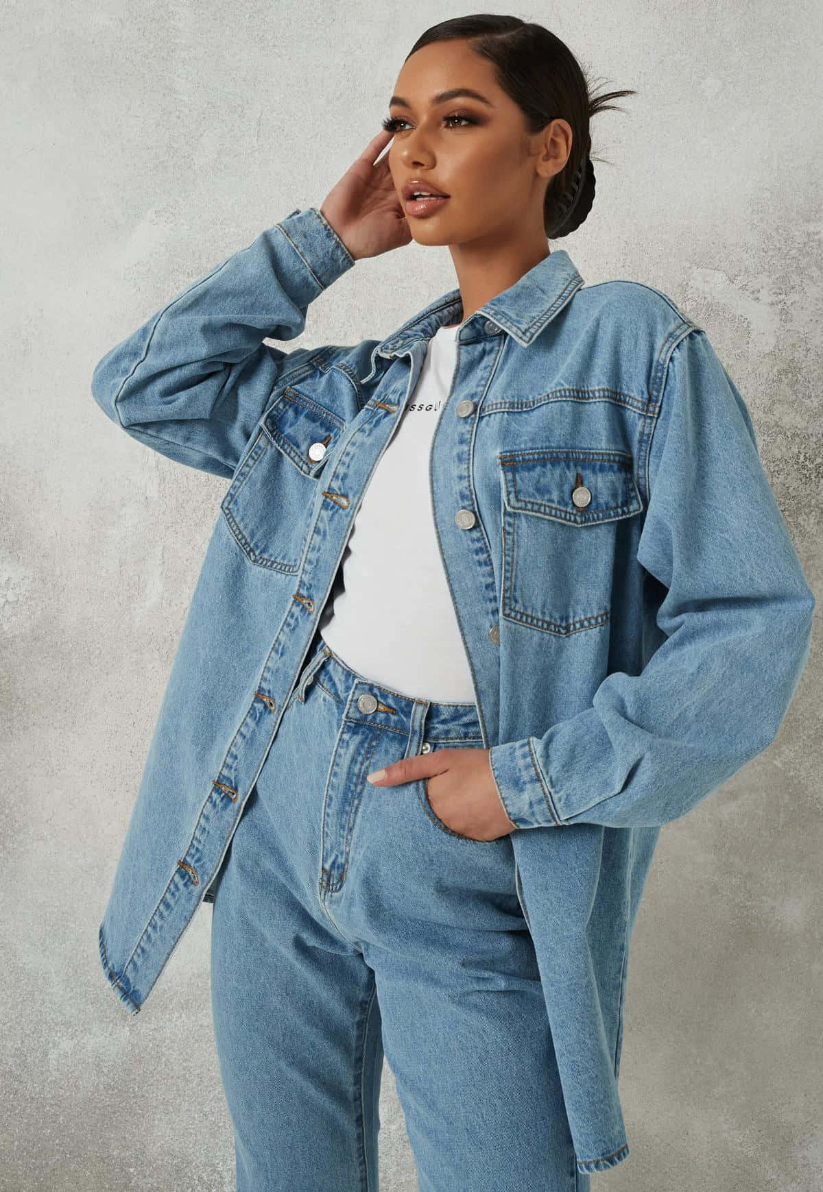 Denim Blue 桌布 壁紙 — 一位身穿淺藍色牛仔外套和牛仔褲的女性，自信地在有紋理的灰色牆壁前擺姿勢。