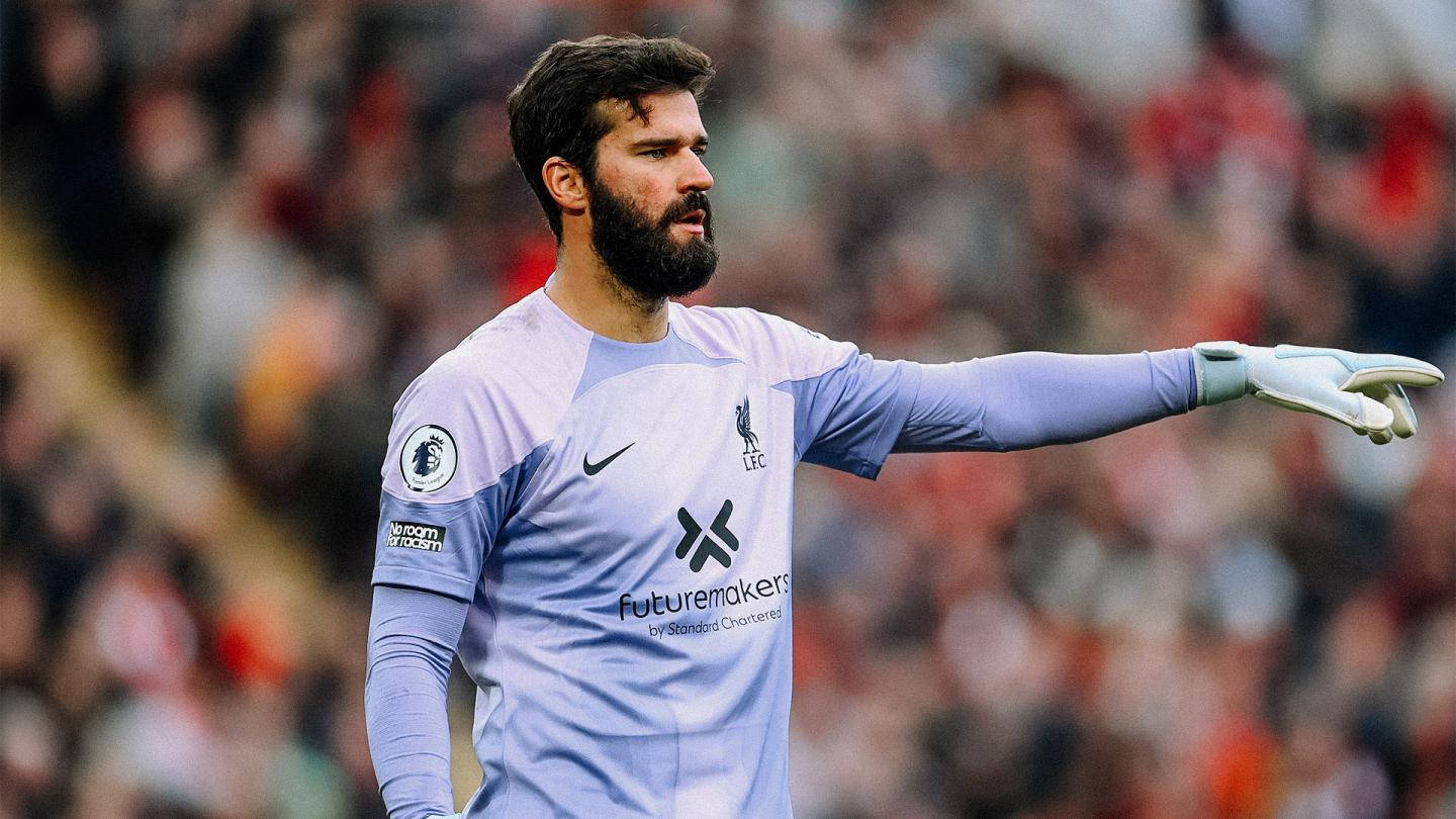 Alisson Becker 桌布 壁紙 — 一位身穿淺藍色球衣、專注的足球守門員在比賽中指揮隊友，身後是模糊的體育場人群。