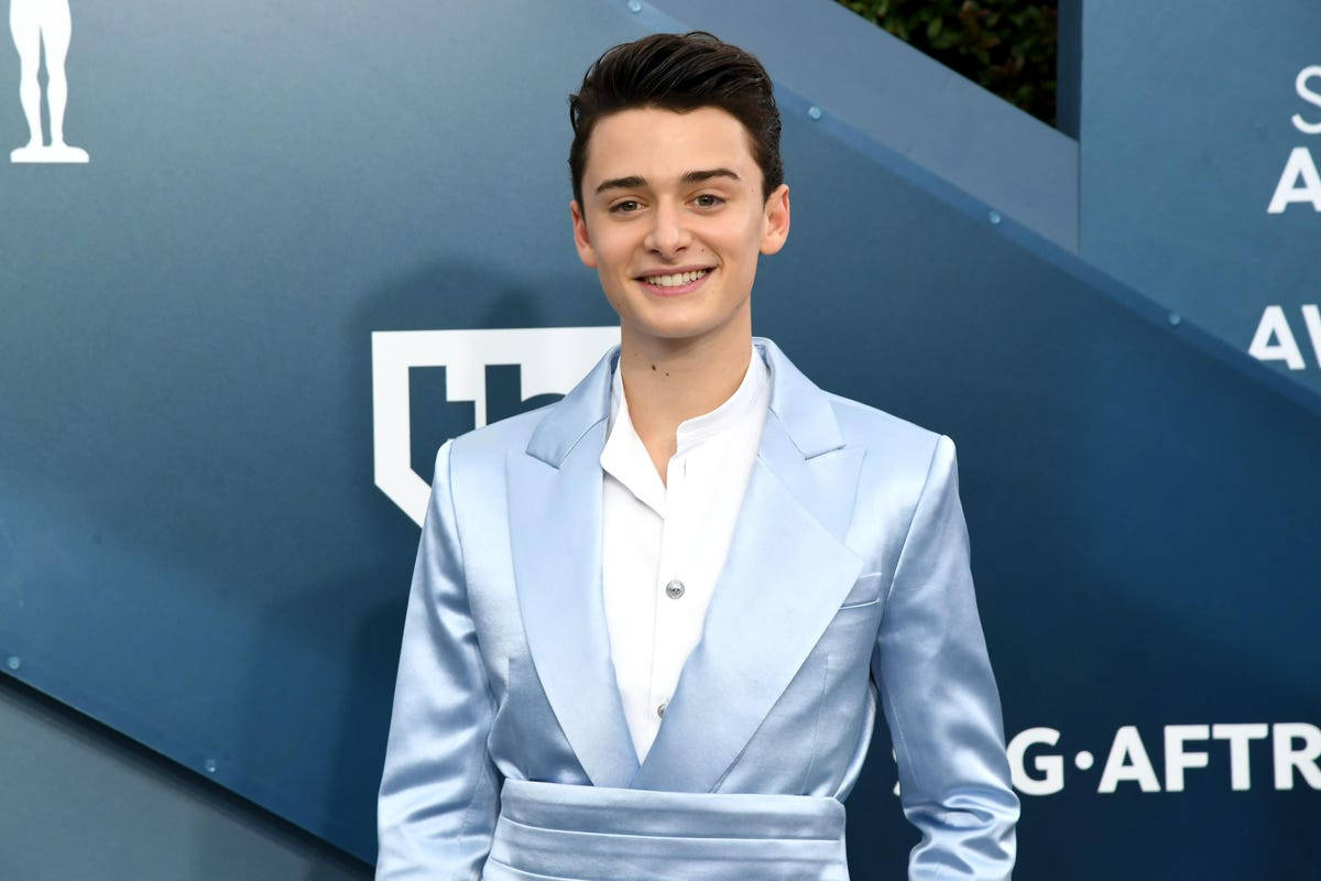 Celebrity 桌布 壁紙 — 一位身穿淺藍色緞面西裝的年輕男子在藍色品牌活動背景前自信地微笑。