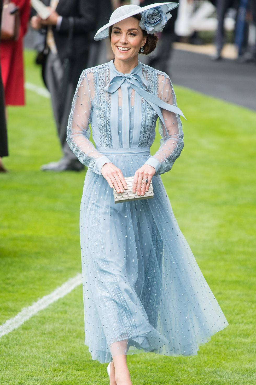 Kate Middleton 桌布 壁紙 — 一位身穿淺藍色蕾絲連衣裙和相配帽子的女士在綠色草坪上微笑行走。