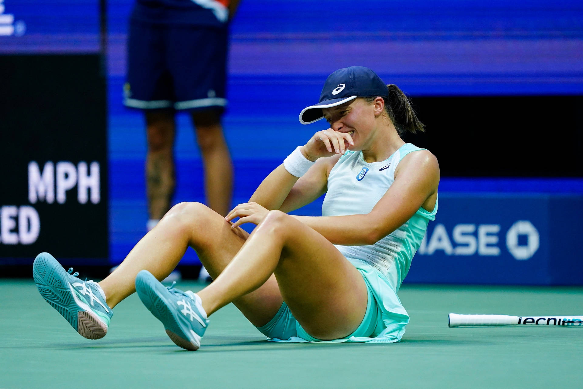 Tennis 桌布 壁紙 — 一位身穿淺藍色裝備的女網球運動員坐在綠色球場上，一手捂臉大笑。