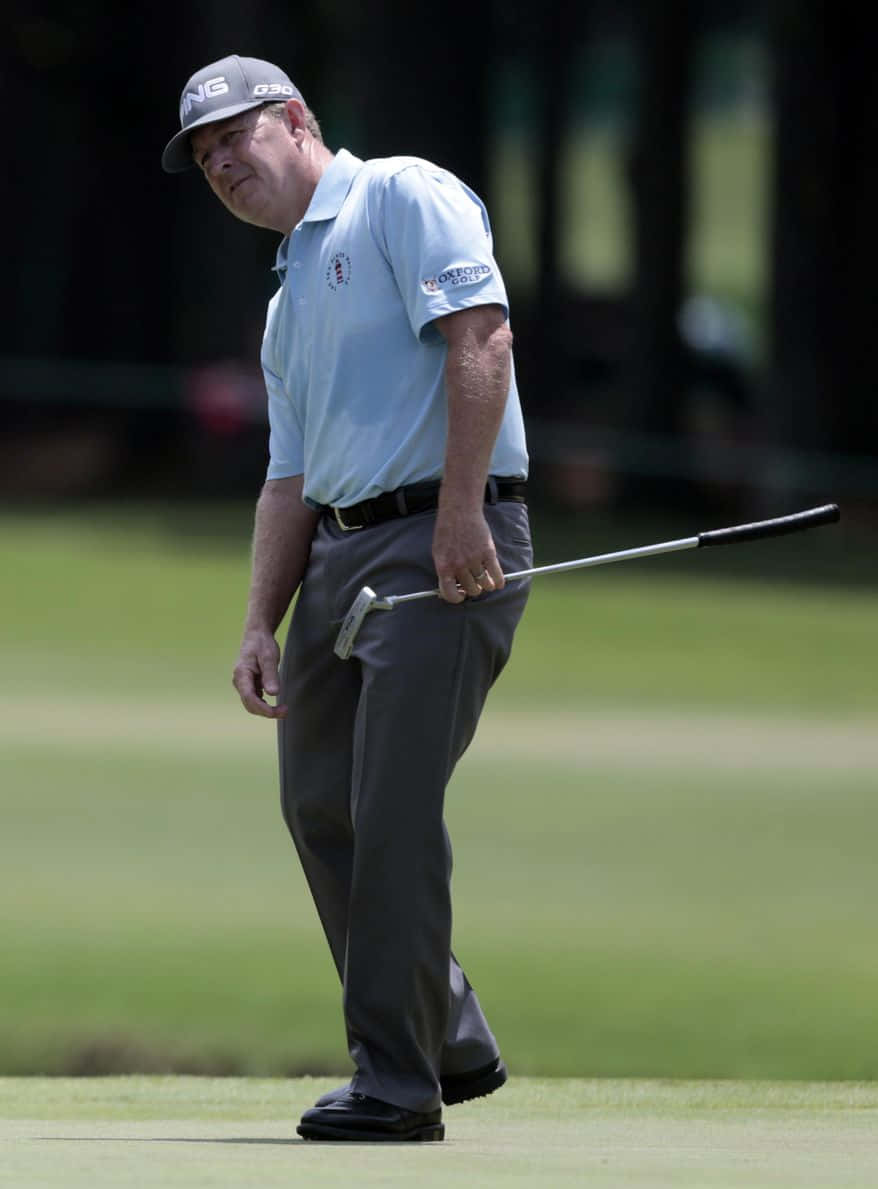 Golf Ball 桌布 壁紙 — 一位身穿淺藍色襯衫和灰色帽子的高爾夫球手，專注地握著推桿，站在綠色的高爾夫球場上。