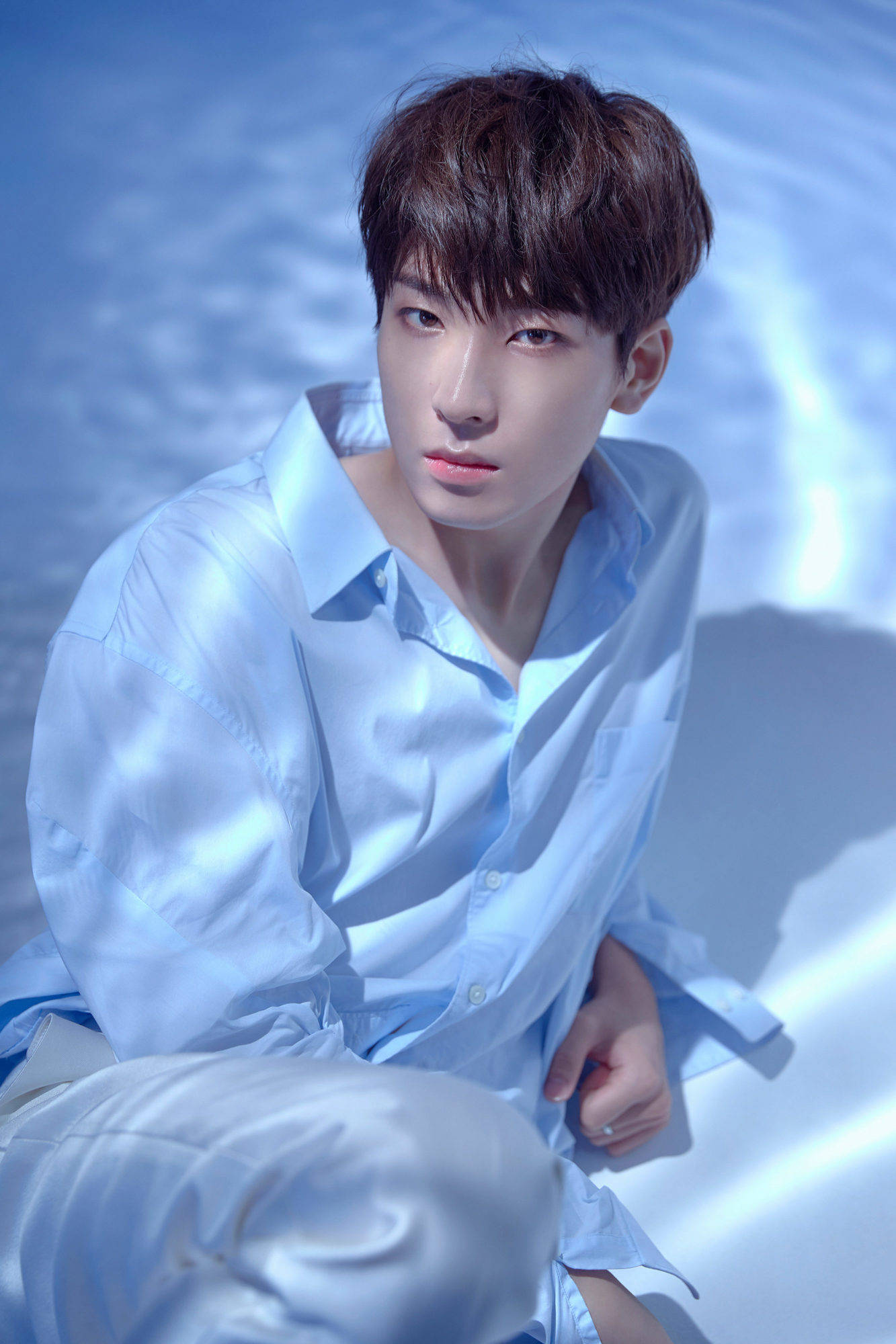 원우 桌布 壁紙 — 一位身穿淺藍色襯衫的年輕男子坐在反射表面上，處於帶有柔和陰影的清涼藍色燈光下。