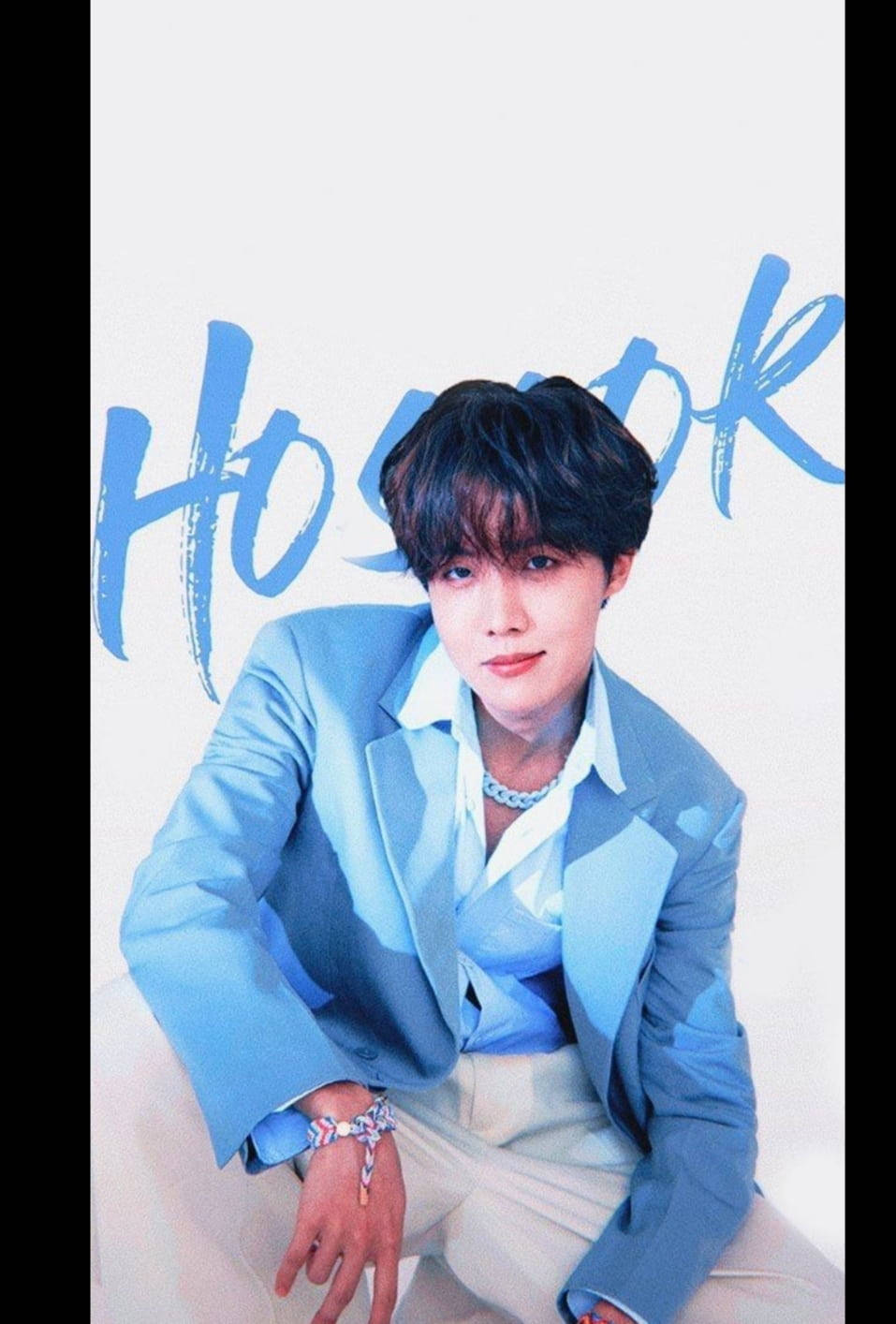 jhope 桌布 壁紙 — 一位身穿淺藍色西裝和奶油色褲子的年輕男子，在白色背景上自信地擺姿勢，背景上有藍色筆觸文字。