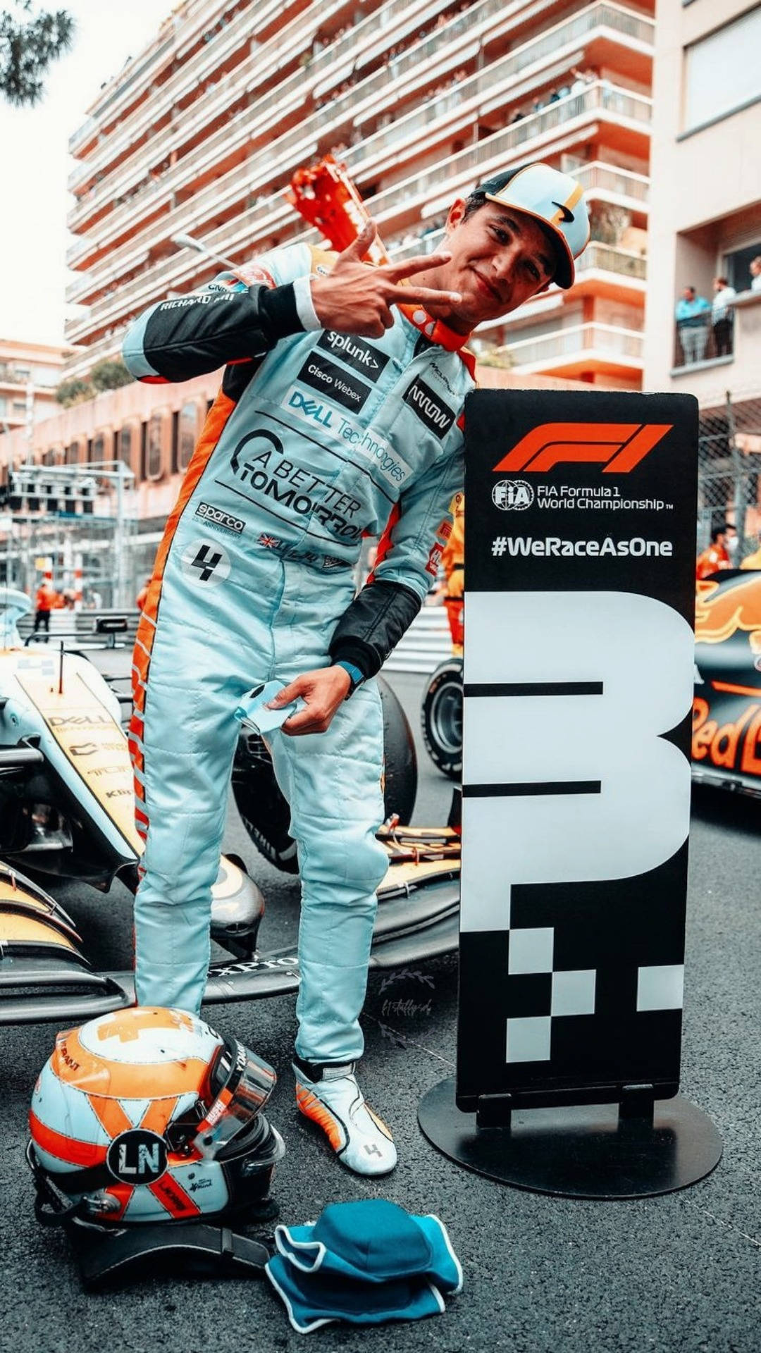Racing 桌布 壁紙 — 一位身穿淺藍色賽車服的F1車手在城市街道上，在他的賽車和品牌標誌旁比出和平手勢。