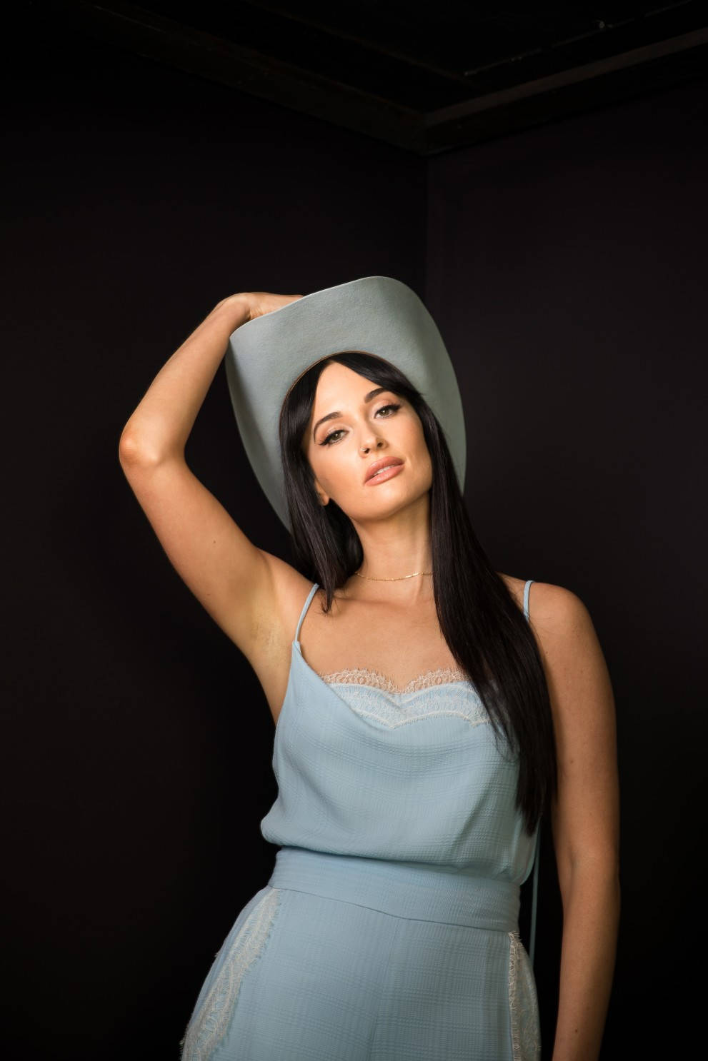 Kacey Musgraves 桌布 壁紙 — 一位身穿淺藍色連衣裙和寬邊帽的女性在黑暗的攝影棚背景下自信地擺姿勢。