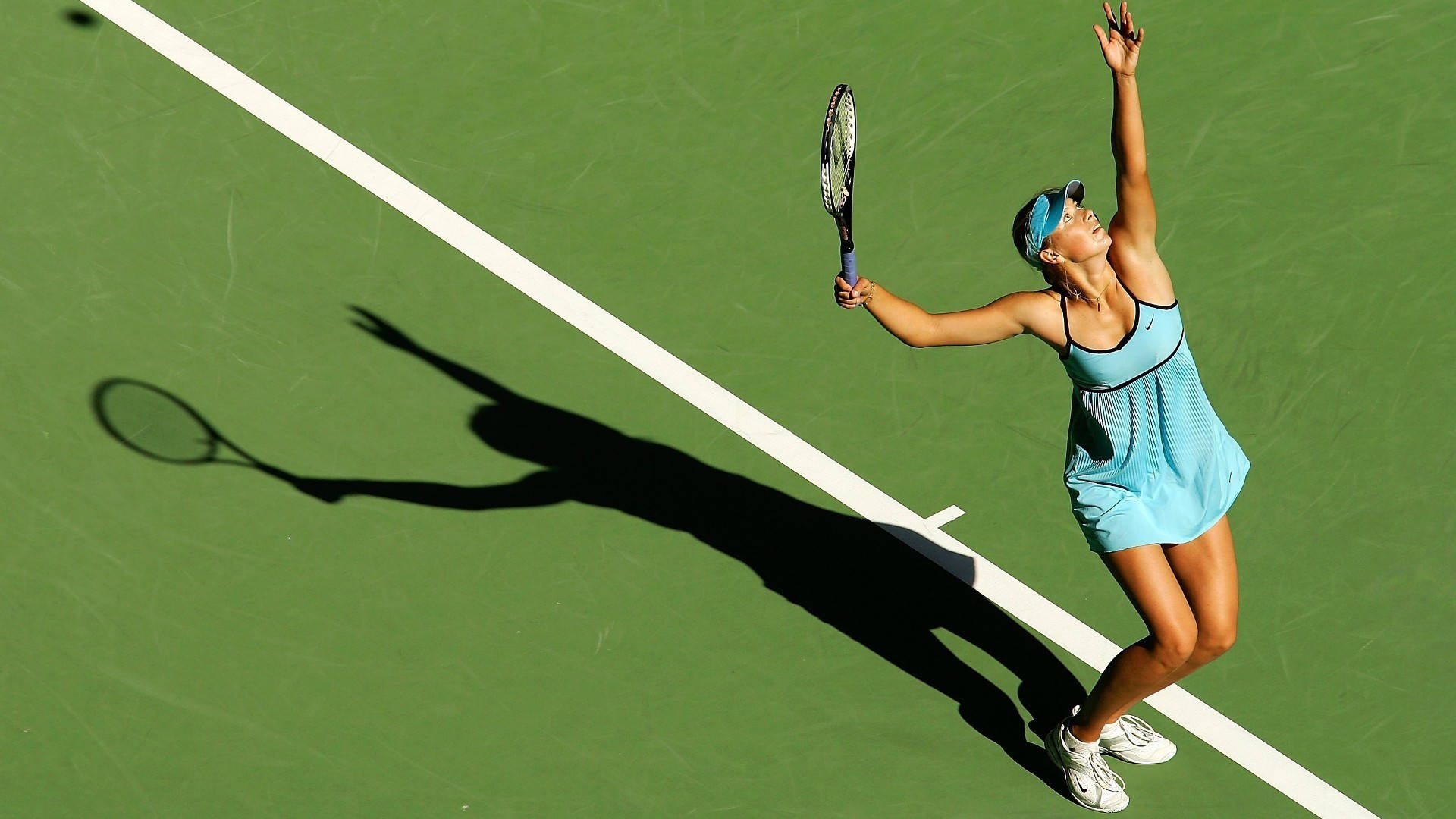 Tennis 桌布 壁紙 — 一位身穿淺藍色連衣裙的女網球選手在綠色球場上跳起發球，她的影子戲劇性地延伸過白線。