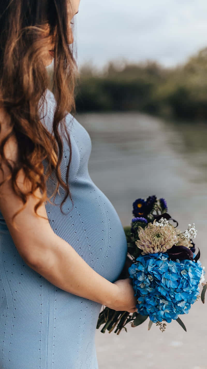 Woman 桌布 壁紙 — 一位身穿淺藍色連衣裙的孕婦，在平靜的河邊，柔和的陰天下，手持一束鮮豔的藍色花束。
