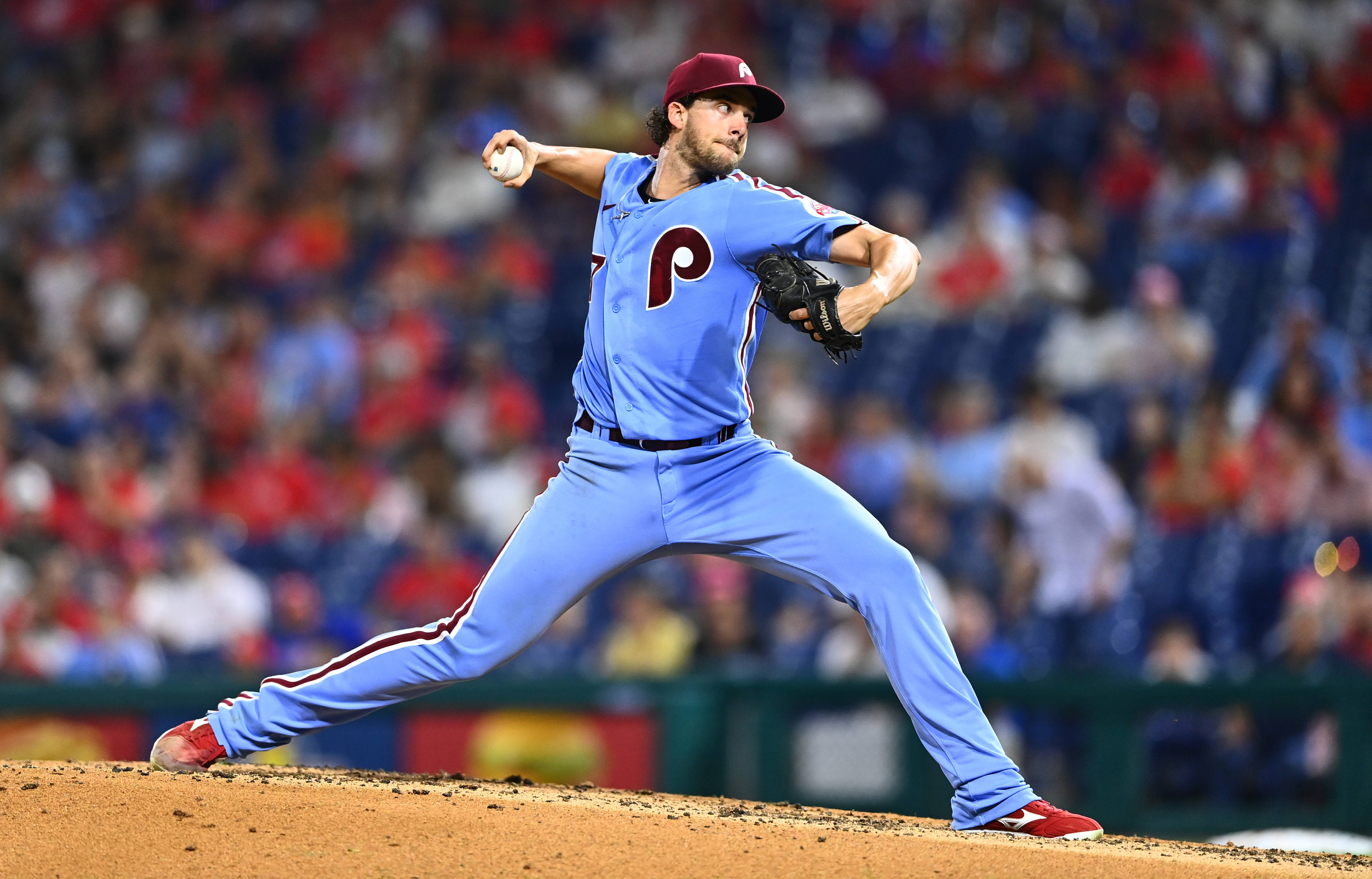 Phillies 桌布 壁紙 — 一位身穿淺藍色配紅色點綴球衣的棒球投手，在球場燈光下的泥土投手丘上投球，背景是模糊的球迷。