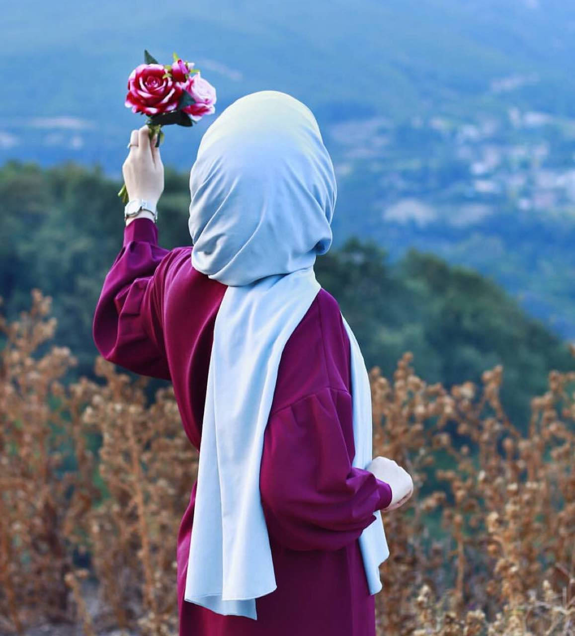 muslim 桌布 壁紙 — 一位身穿淺藍色頭巾和栗色長袍的女性站在山坡上，手持一束粉紅玫瑰，背景是朦朧的山巒。