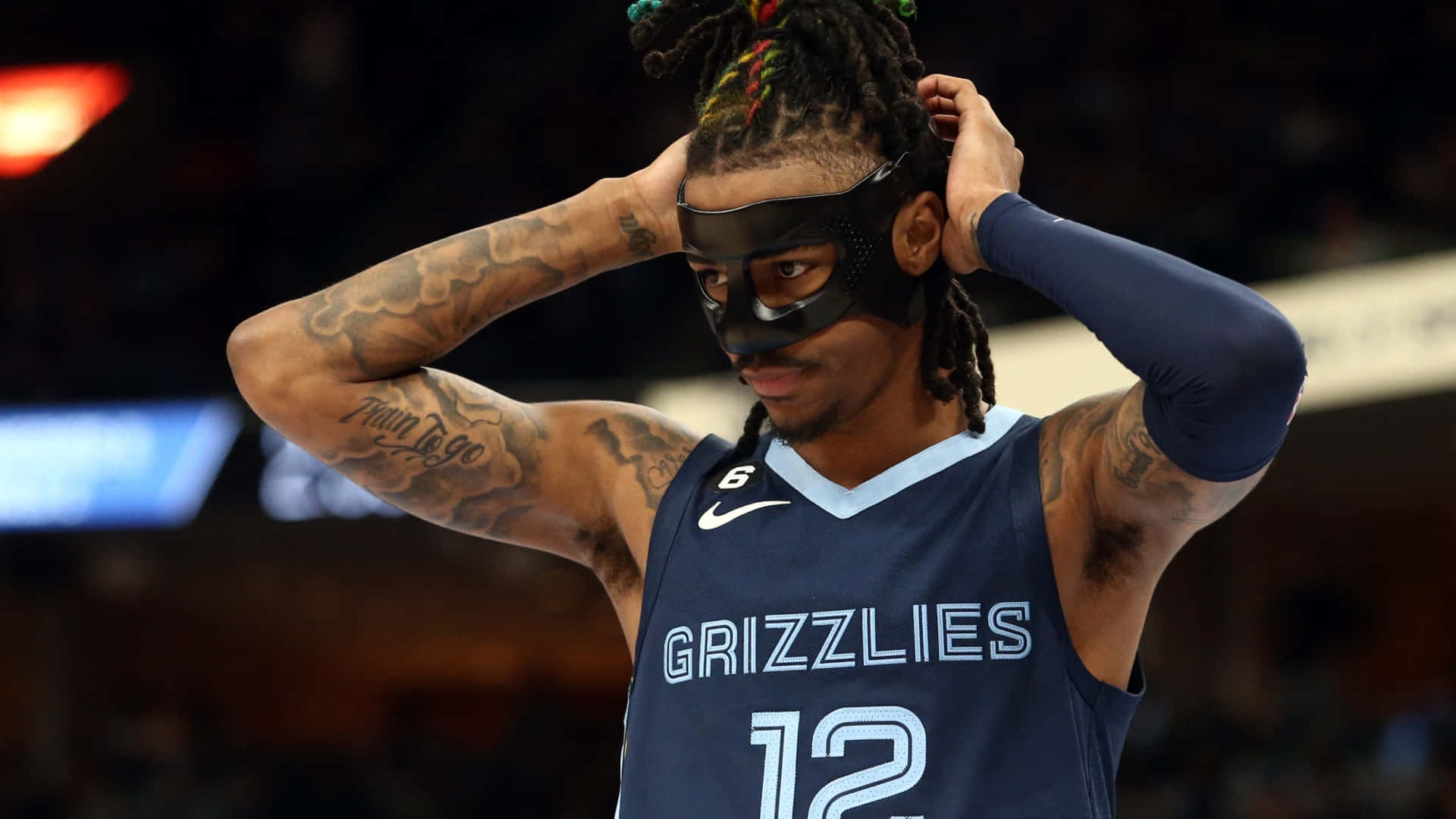 Ja Morant 動圖 桌布 壁紙 — 一位身穿灰熊隊球衣的籃球運動員在明亮的場館燈光下站在球場上，調整黑色面罩。