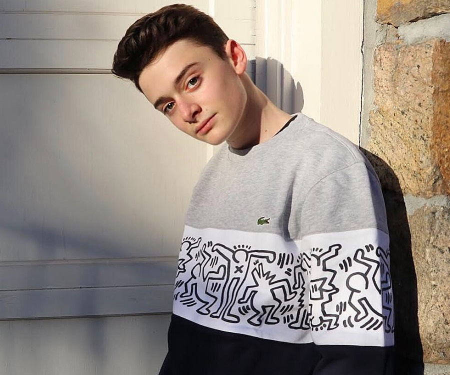 Celebrity 桌布 壁紙 — 一位身穿灰色和黑色連帽衫、帶有Keith Haring風格圖案的年輕男子，在柔和陽光下靠著石牆。