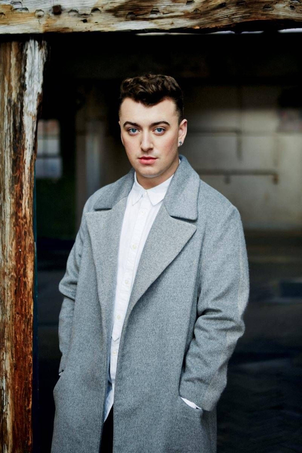 Sam Smith 桌布 壁紙 — 一位身穿灰色外套的年輕男子自信地站在風化的木門框內，雙手插在口袋裡。
