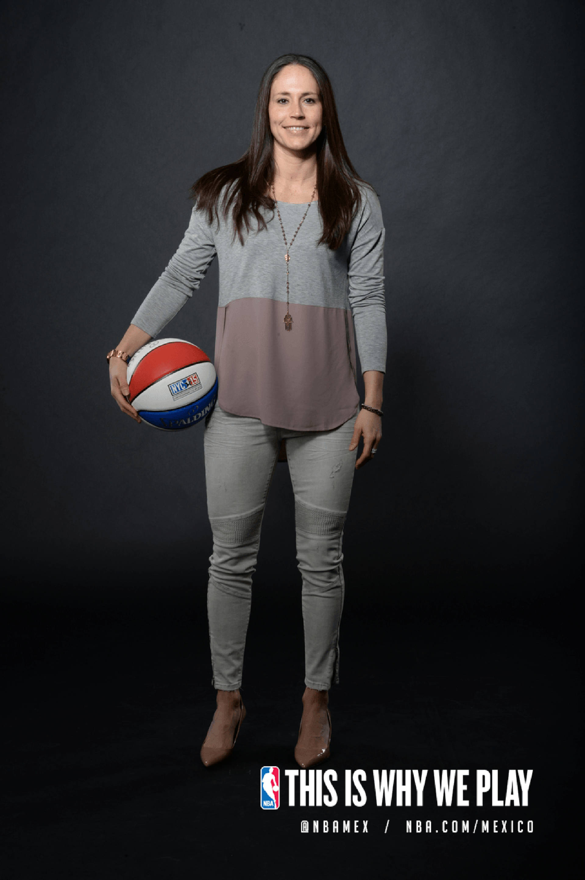 Sue 桌布 壁紙 — 一位身穿灰色服裝的微笑女性，在帶有NBA Mexico品牌標誌的深色工作室背景下拿著籃球。