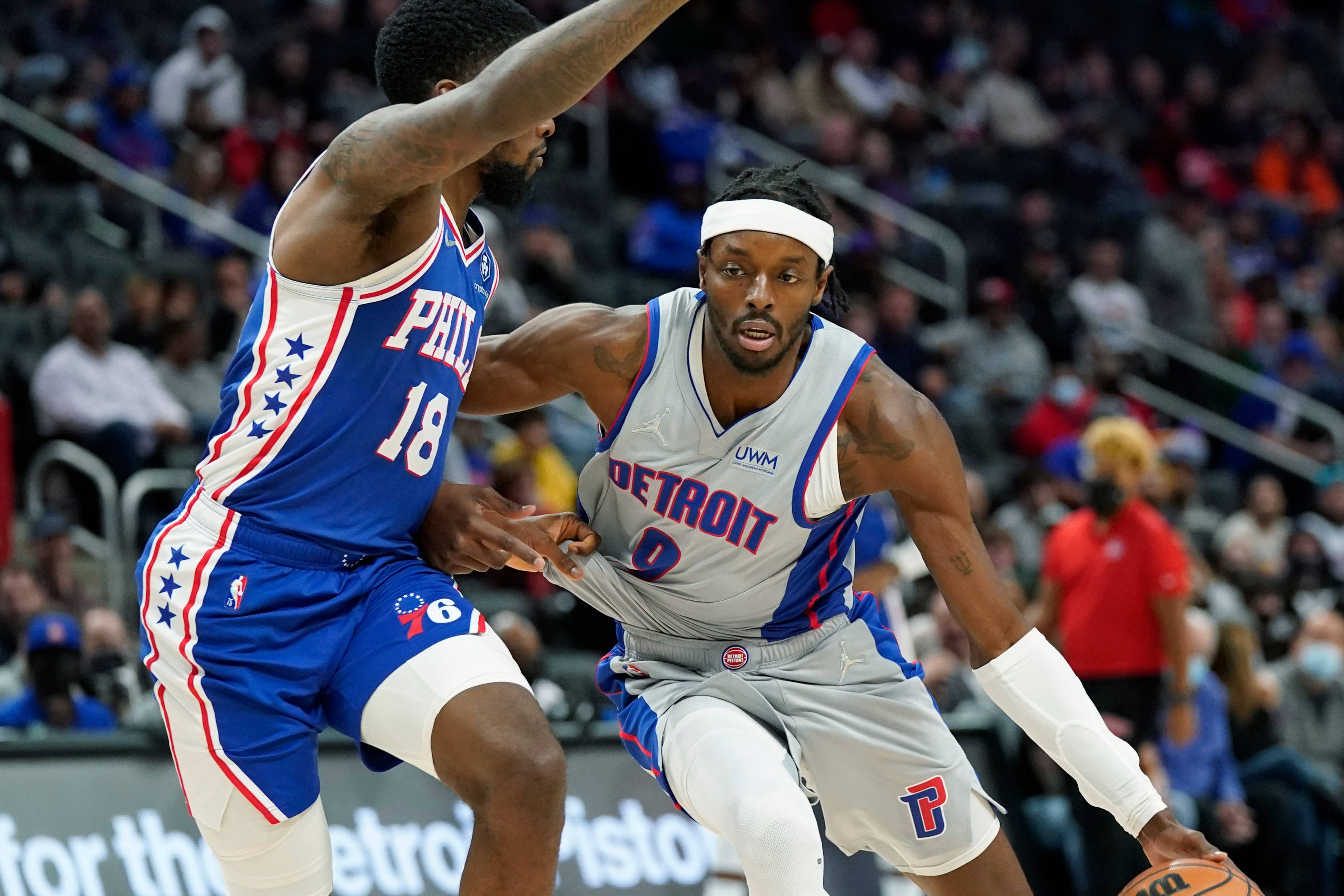 76ers 桌布 壁紙 — 一位身穿灰色球衣的底特律活塞隊球員在籃球比賽中運球，同時被一位身穿藍色球衣的費城76人隊球員緊密防守。