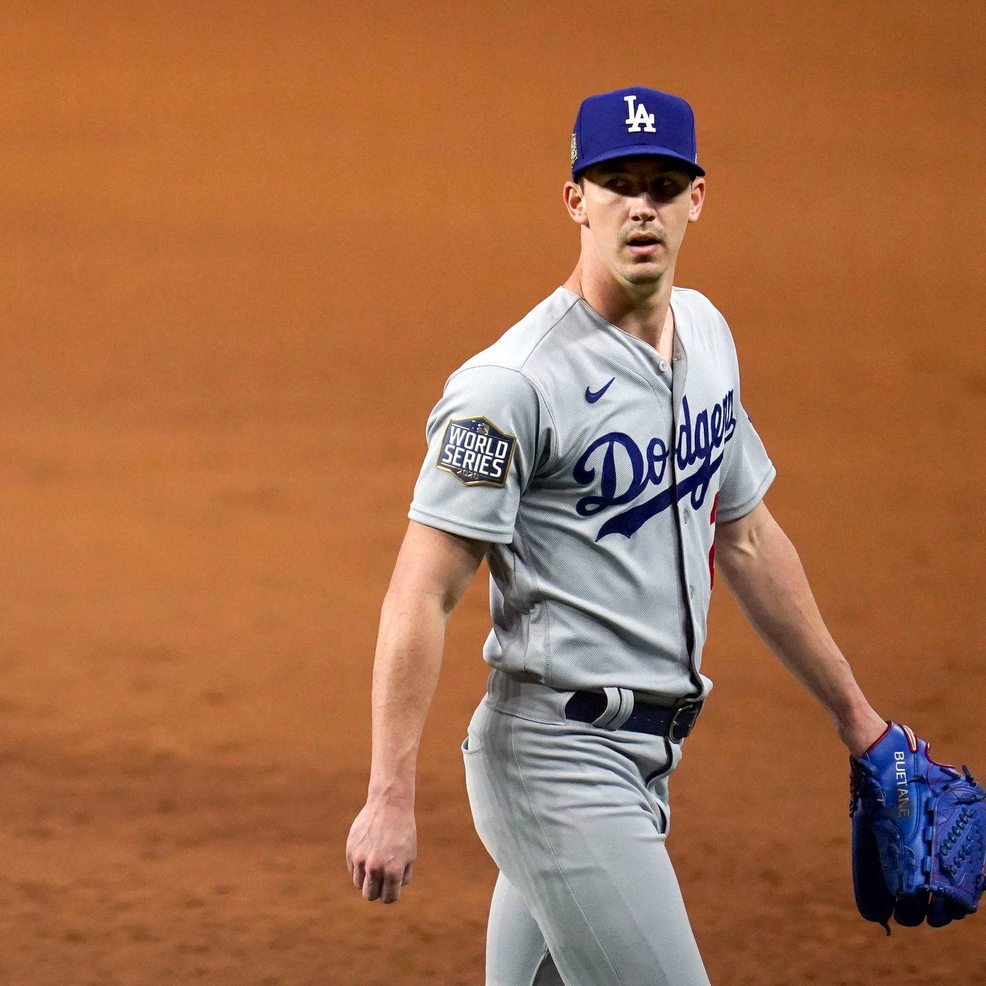 walker buehler 桌布 壁紙 — 一位身穿灰色球衣的洛杉磯道奇棒球選手在球場燈光下走在泥地球場上。
