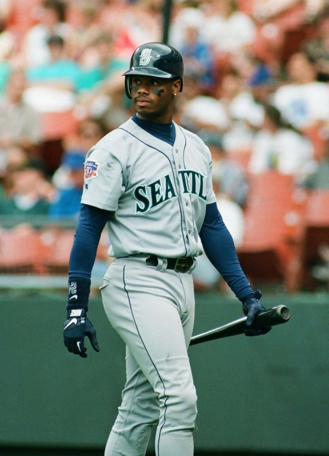 baseball bat 桌布 壁紙 — 一位身穿灰色球衣的西雅圖水手隊棒球選手手持球棒，在模糊觀眾背景的球場上行走。