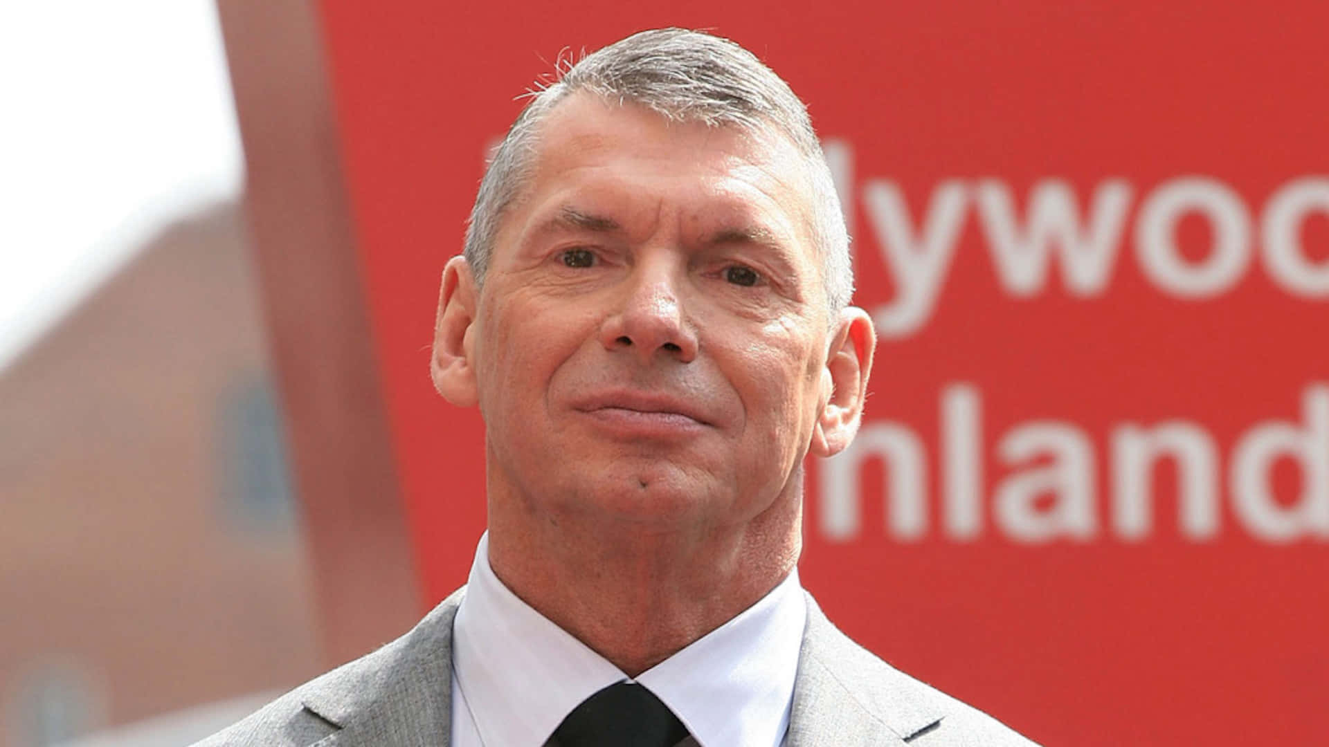 WWE 桌布 壁紙 — 一位身穿灰色西裝和黑色領帶的男子站在紅色好萊塢芬蘭標誌前的特寫肖像。