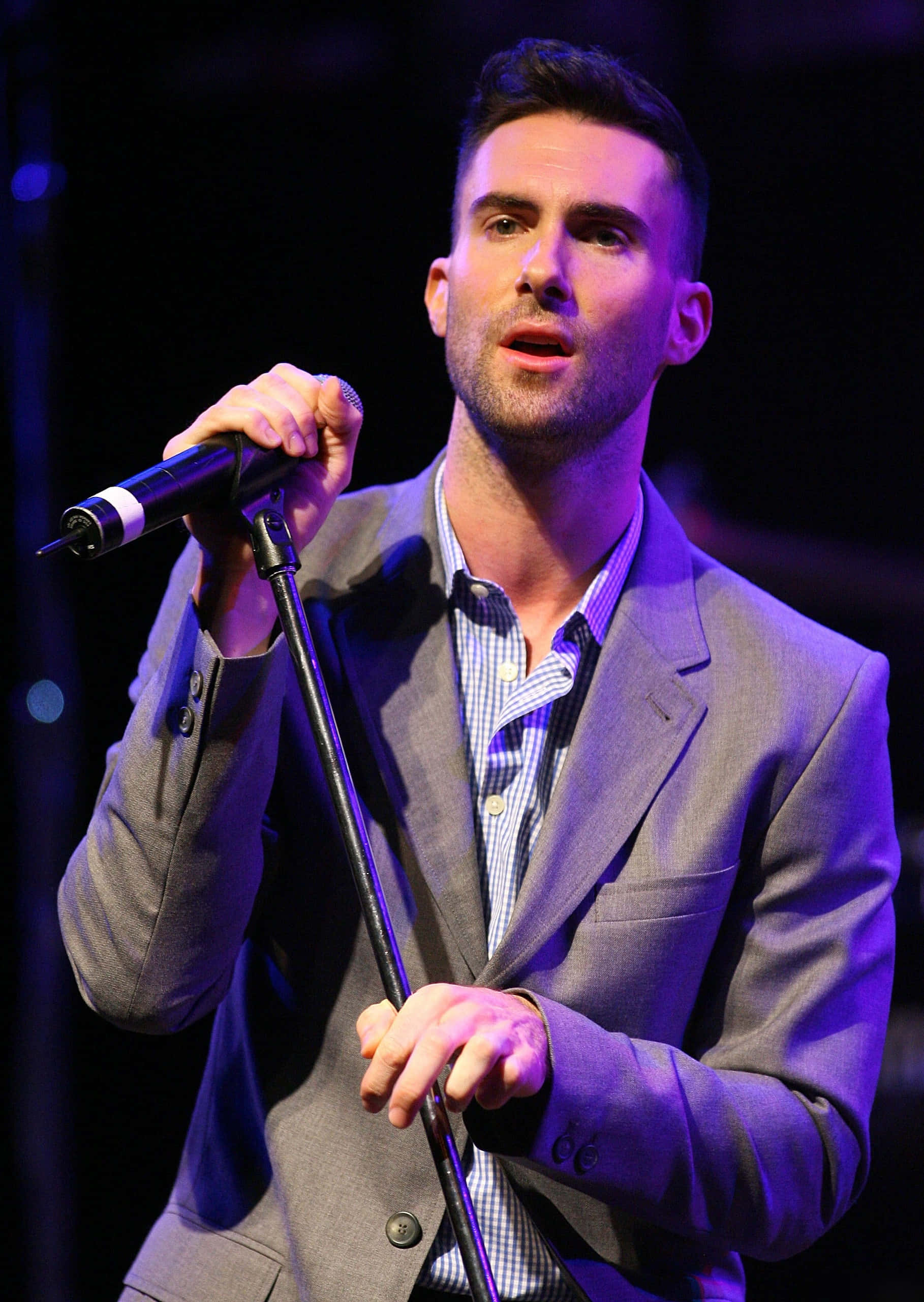 Adam Levine 桌布 壁紙 — 一位身穿灰色西裝的男歌手在充滿活力的紫色舞台燈光下，熱情地對著麥克風演唱。