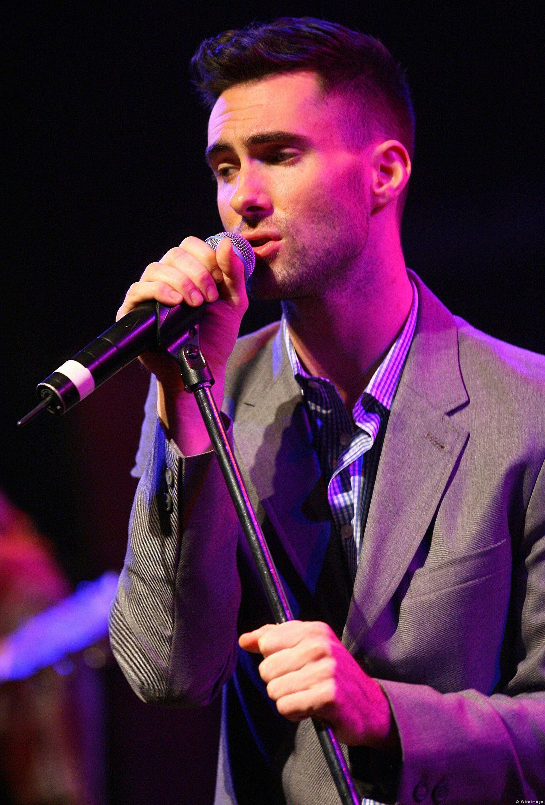 Adam Levine 桌布 壁紙 — 一位身穿灰色西裝的男歌手在充滿活力的紫色舞台燈光下，對著麥克風深情演唱。