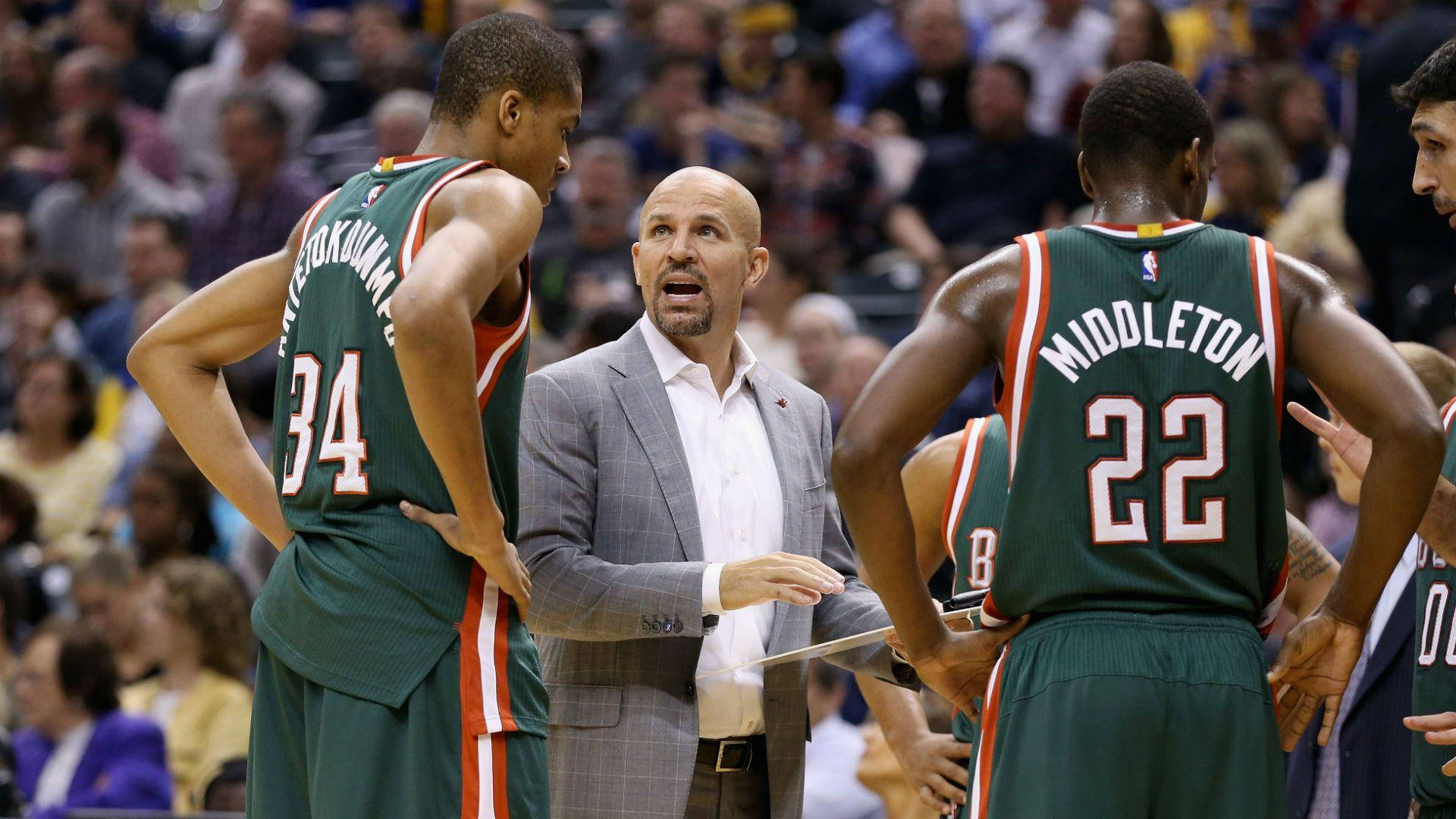 NBA 桌布 壁紙 — 一位身穿灰色西裝的籃球教練在比賽中熱情地與兩名身穿綠色球衣的球員交談，背景是模糊的人群。