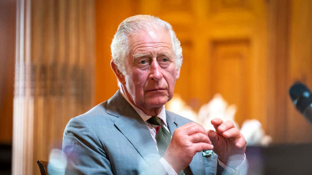 Politics 桌布 壁紙 — 一位身穿灰色西裝的長者坐在室內，雙手緊握，在溫暖的木質背景下表情嚴肅。