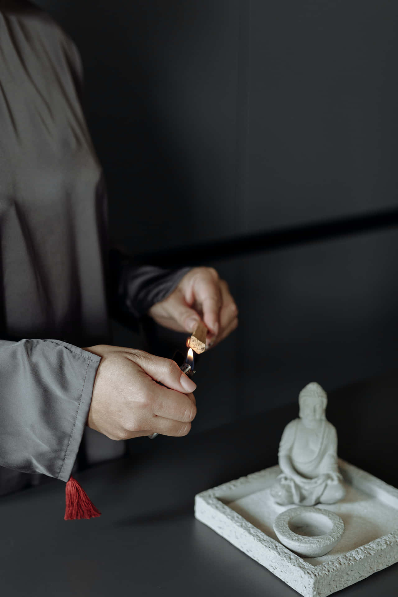 佛陀 桌布 壁紙 — 一位身穿灰色長袍的人，在一個有紋理的托盤上，於寧靜的白色佛像旁點燃蠟燭。